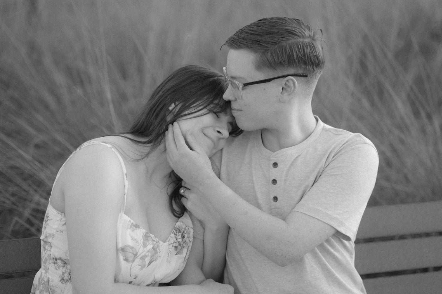 Black and white photo of a romantic couple sharing a tender moment outdoors near tall grass.