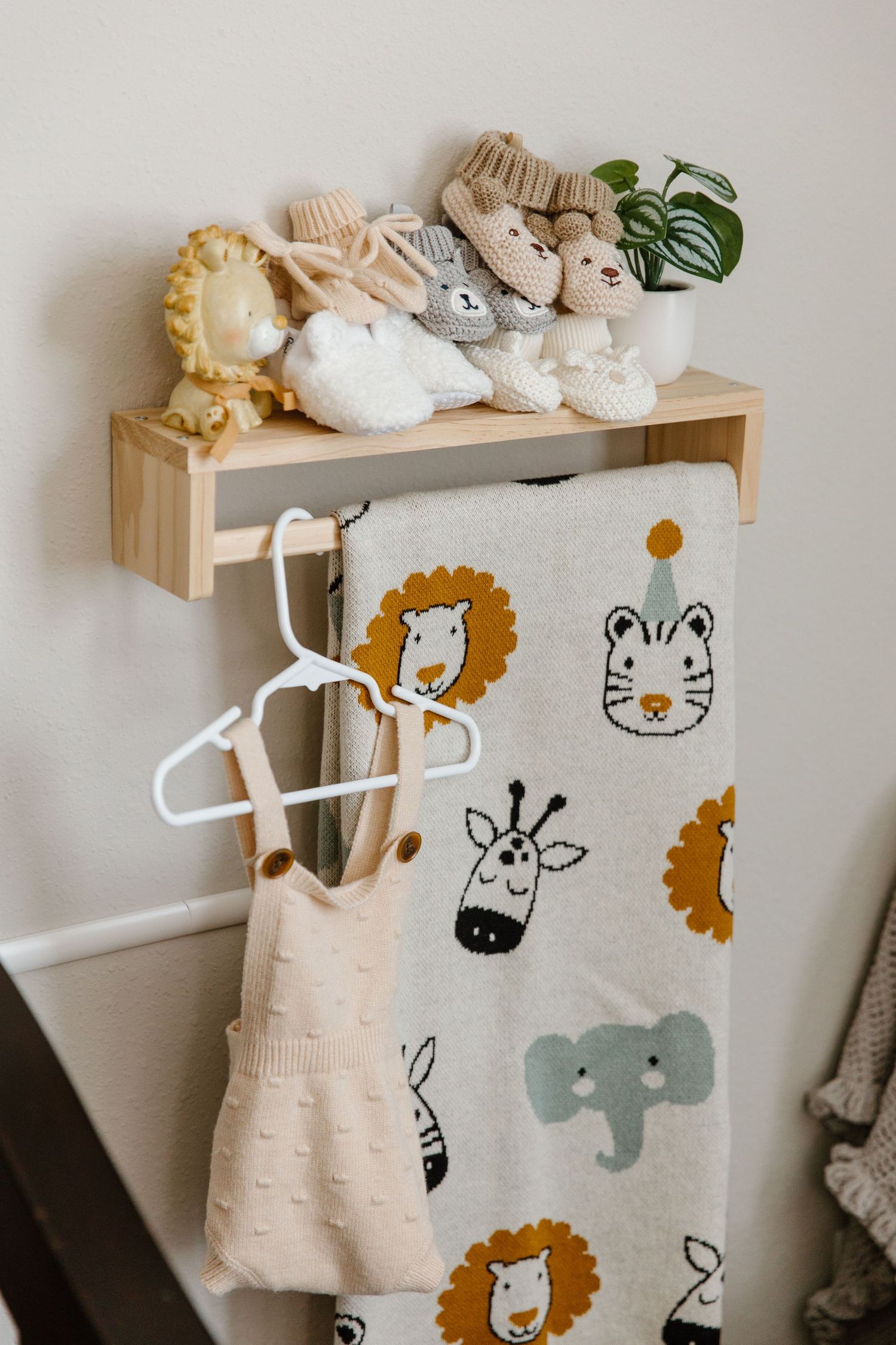 A nursery wall decorated with cute animal decals features a small wooden shelf and hanging baby clothes in neutral tones.