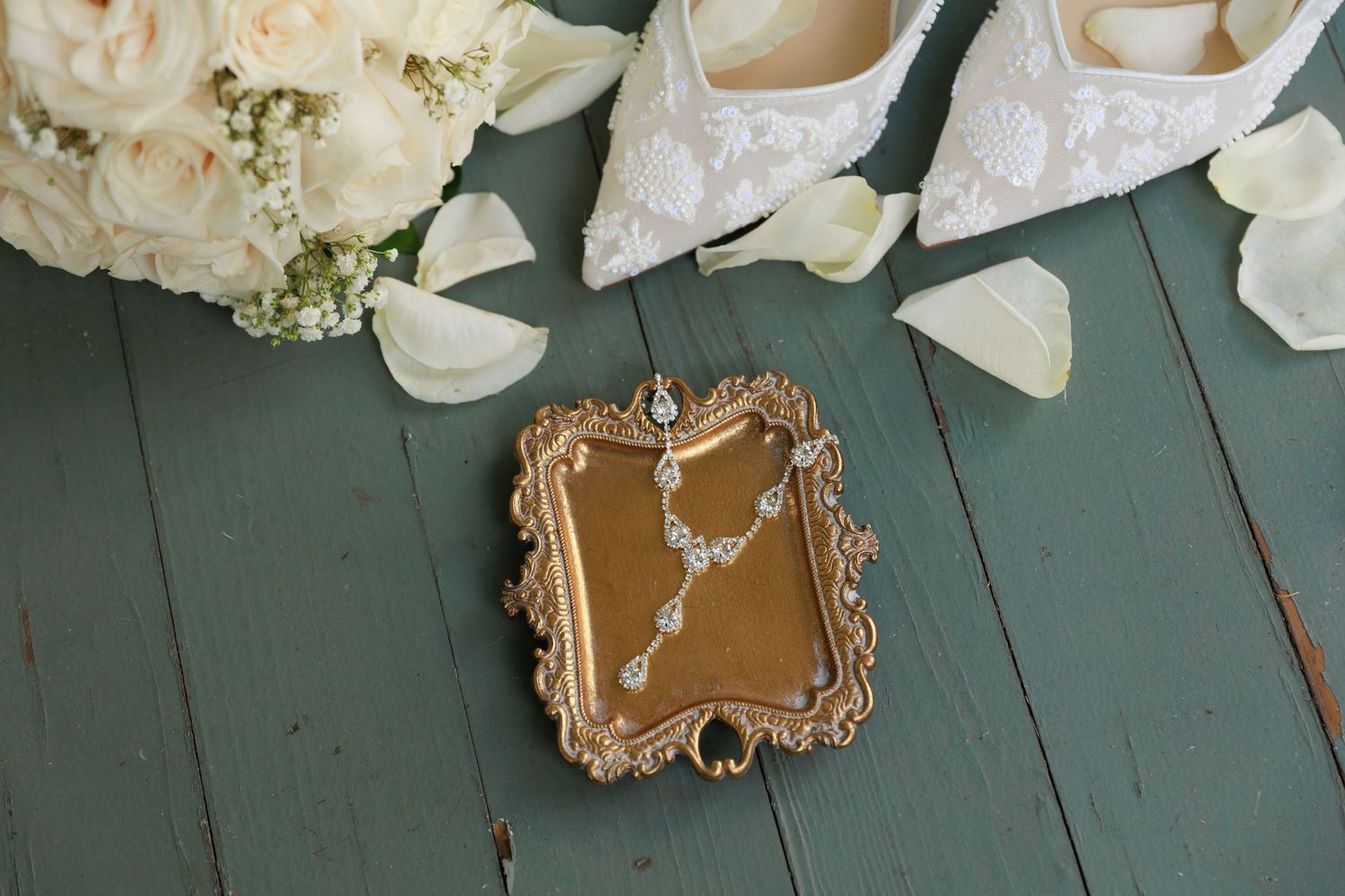 White wedding shoes and delicate floral arrangements displayed on a rustic green wooden surface.
