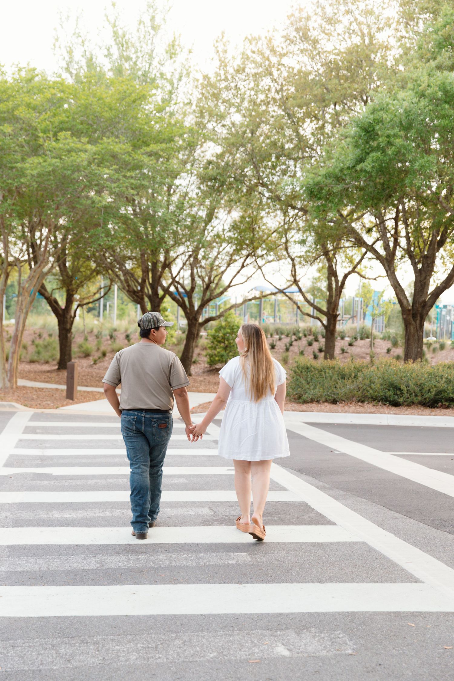 Couple holding hands walking across a crosswalk, man in gray shirt and jeans, woman in white dress.