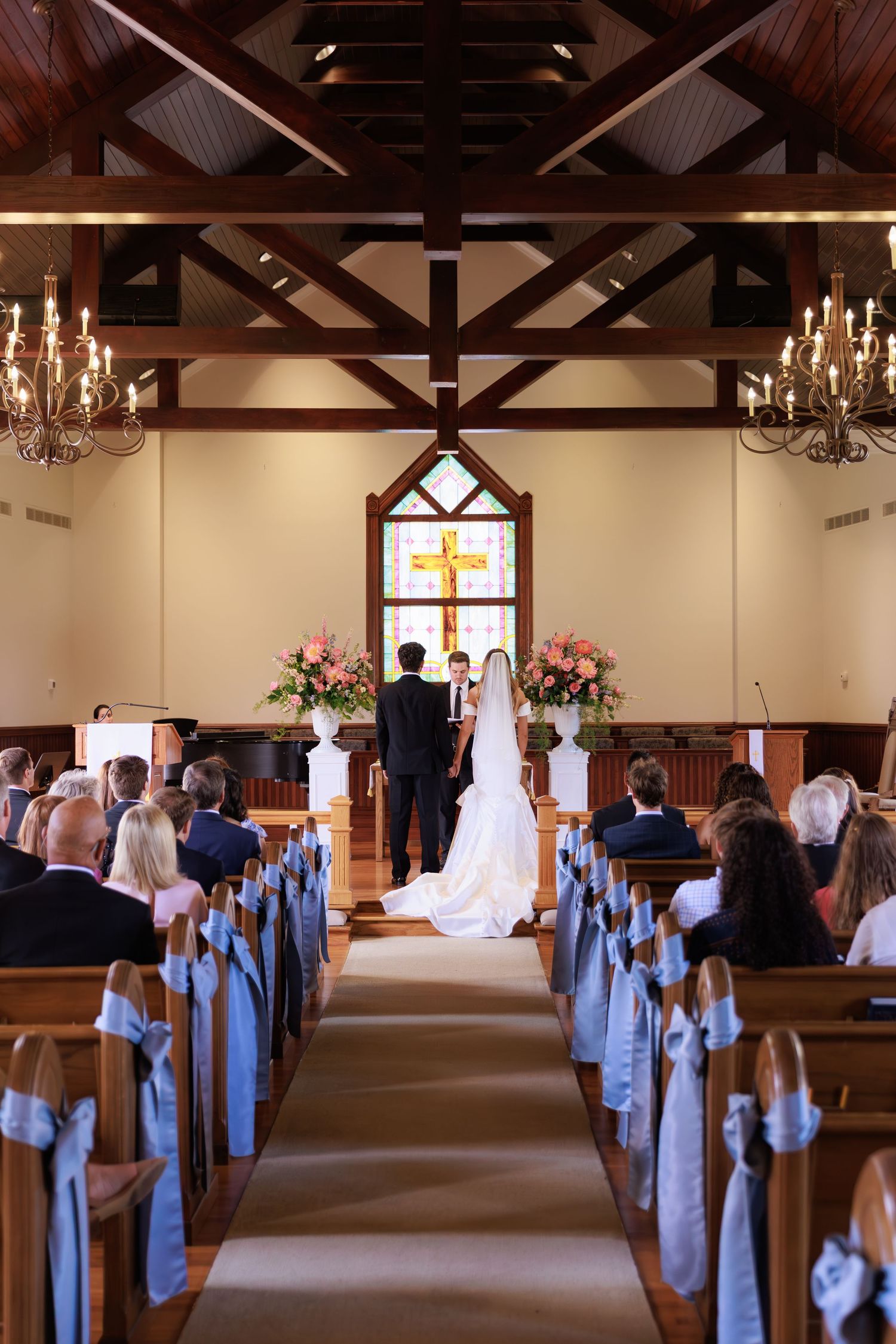 A traditional church wedding ceremony takes place in a chapel with exposed wooden beams and crystal chandeliers.