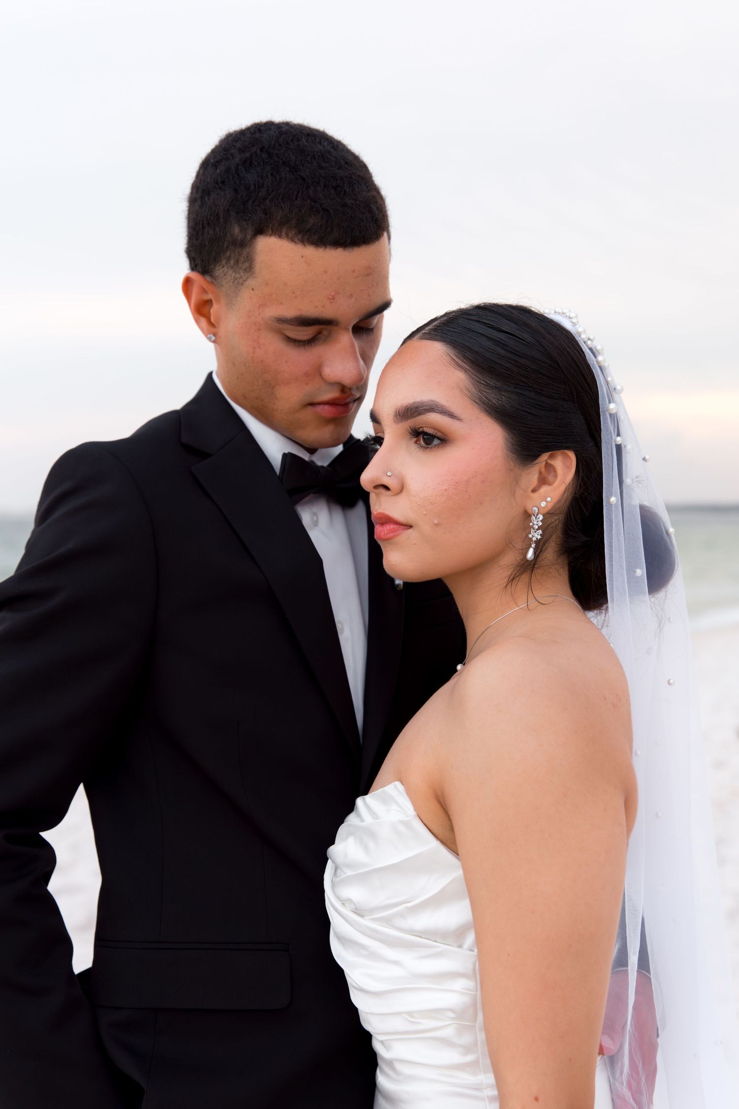 Close-up wedding portrait of couple against ocean backdrop.