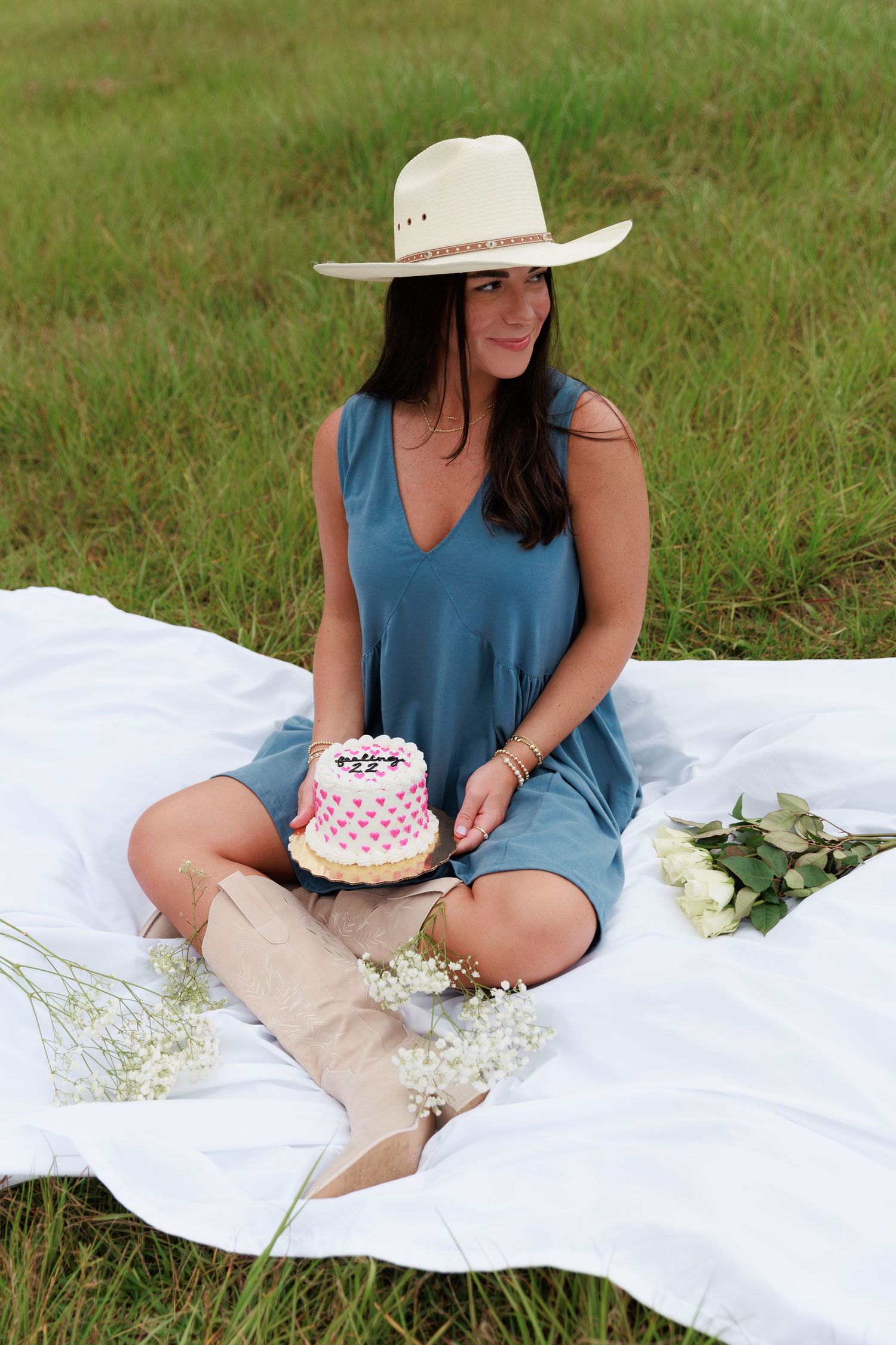 Picnic scene with cake, white blanket, and country-inspired fashion in an open field.