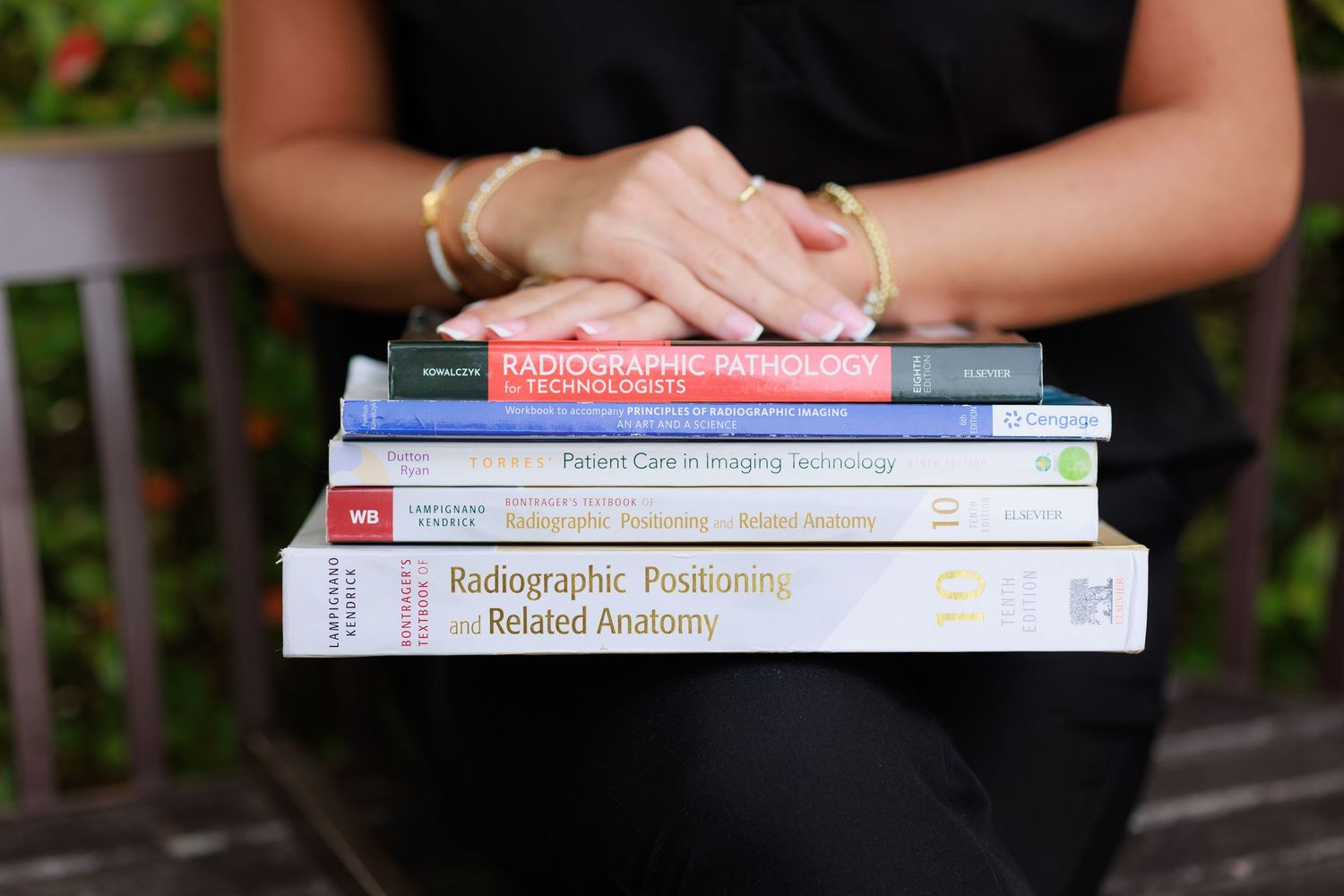 Student holding a stack of radiographic positioning and imaging technology textbooks outdoors.