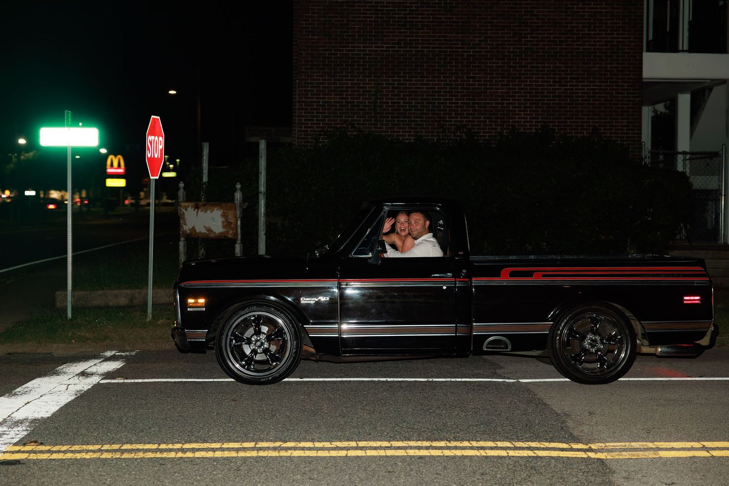 Black pickup truck parked at night on a street corner near a McDonald's sign and stop sign.
