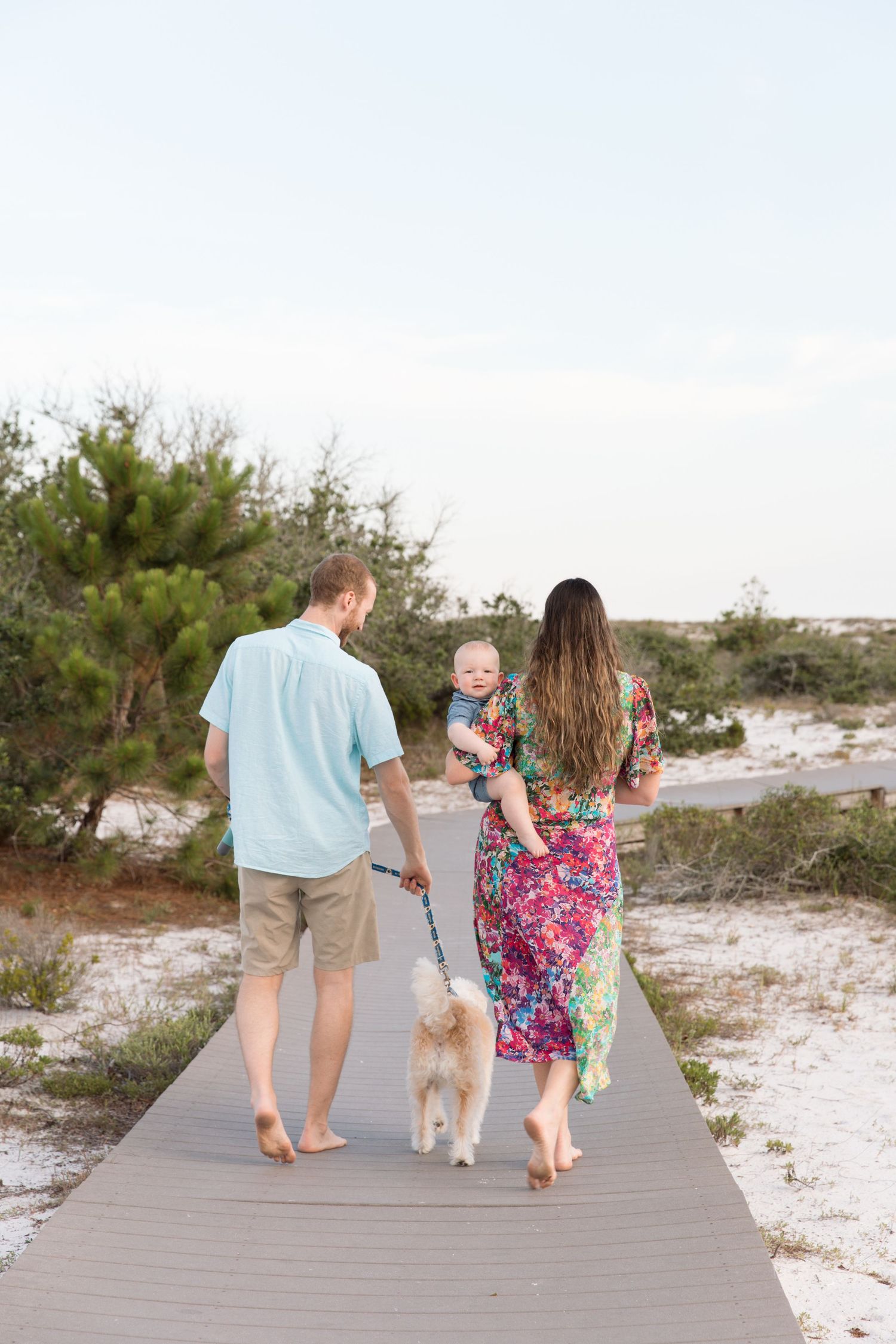 Family and their golden retriever walking together on a wooden boardwalk at the beach during sunset.