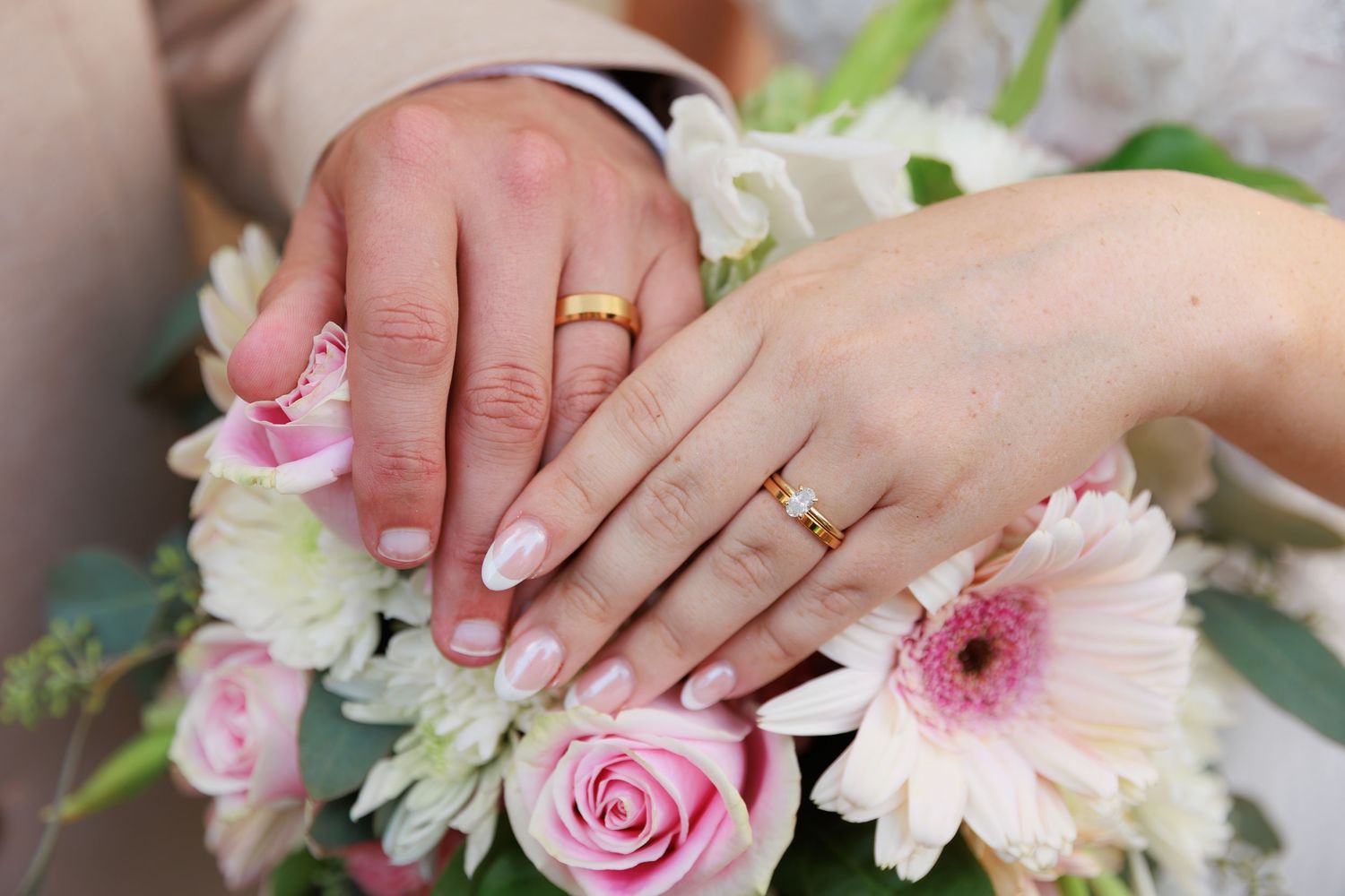 Close-up of hands arranging pink and white flowers in a delicate floral arrangement with roses and gerbera daisies.