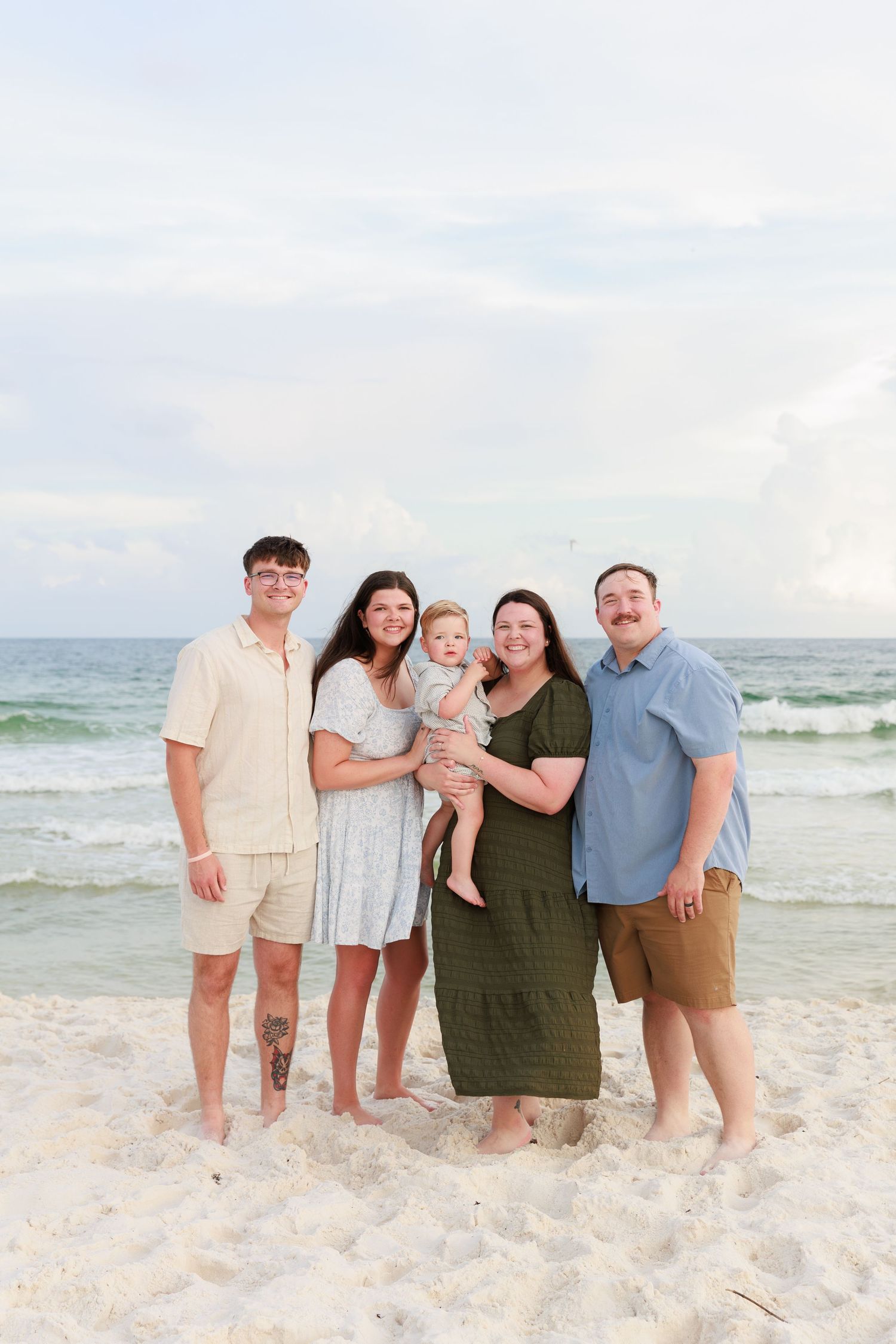 A group stands together on a white sandy beach at sunset with ocean waves in the background.