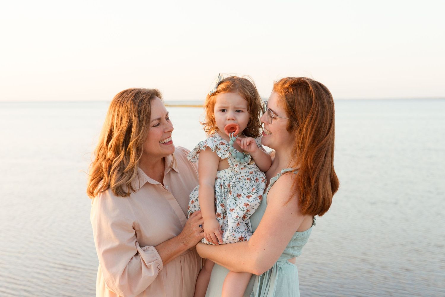 A family shares tender moments together while walking along a sandy beach at sunset.