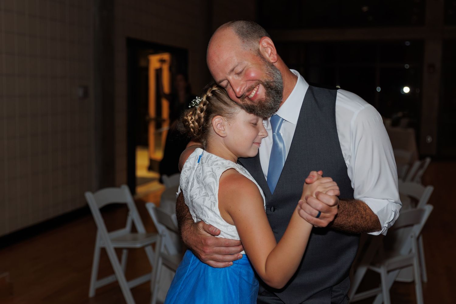 Father and daughter share emotional moment during wedding dance on wooden dance floor.
