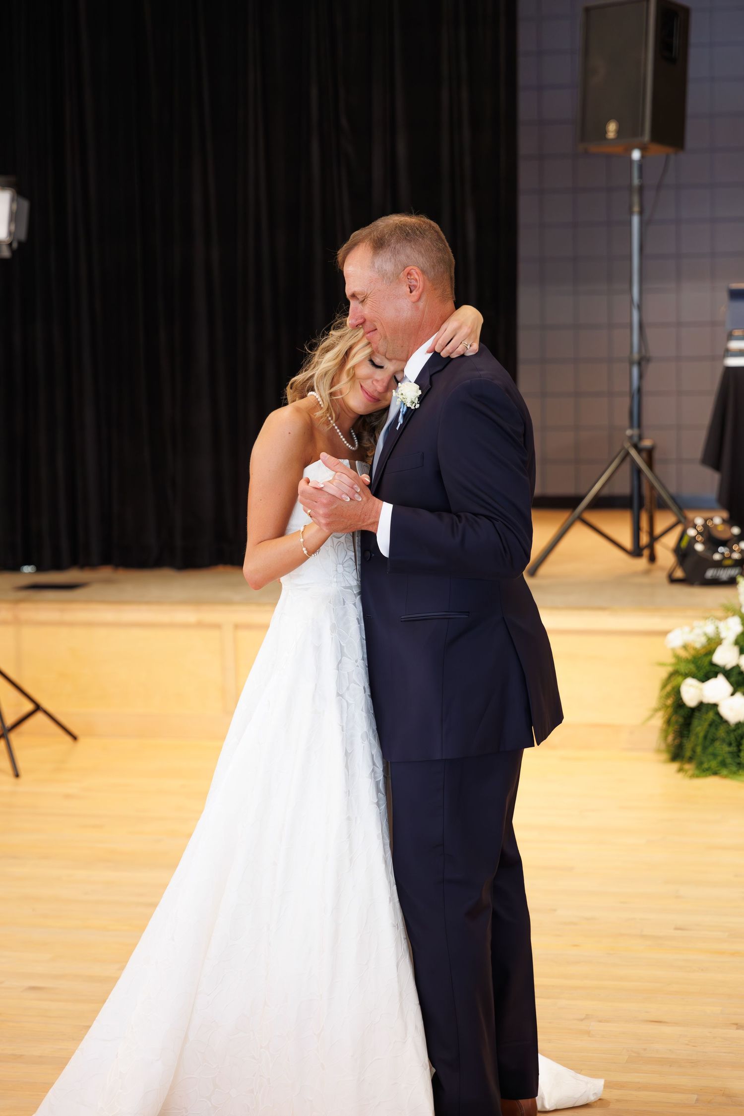 Intimate slow dance moment at wedding reception with white floral decorations.