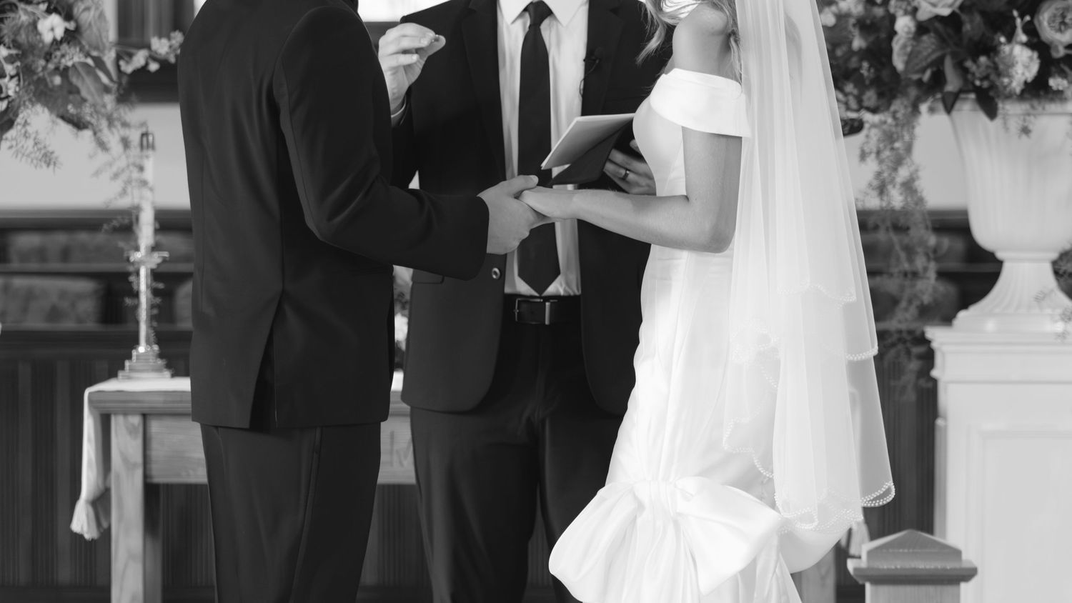 A black and white photo captures a traditional wedding ceremony exchange between a bride and officiant.