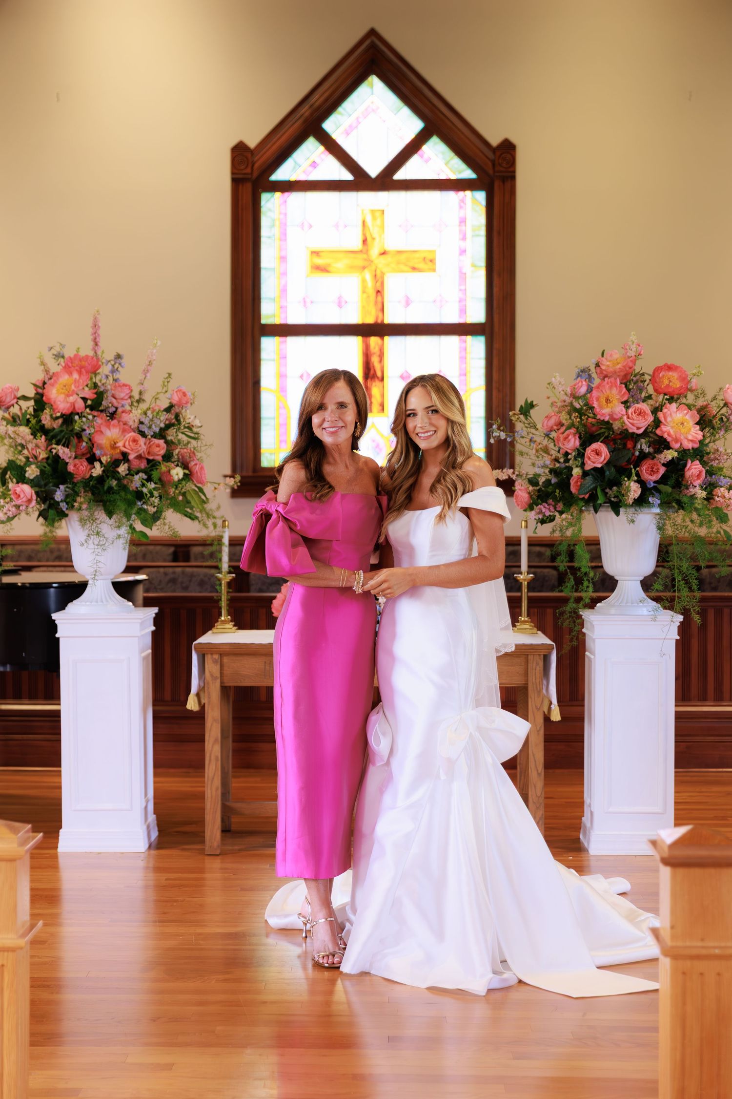 Wedding party members in white and pink dresses posing for creative photos in a church with floral decorations.