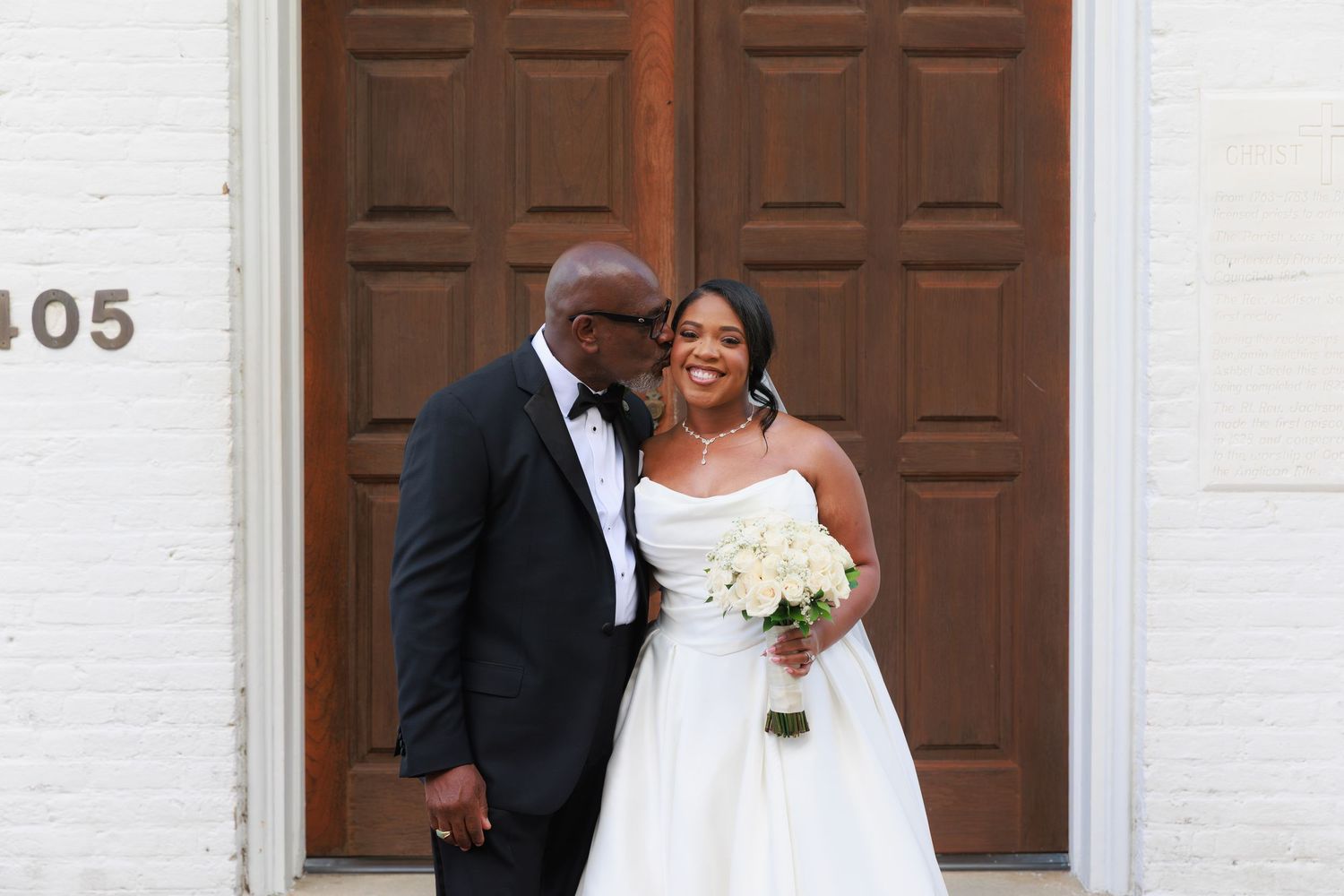 A bride and groom share a romantic moment in front of wooden church doors during their wedding ceremony.