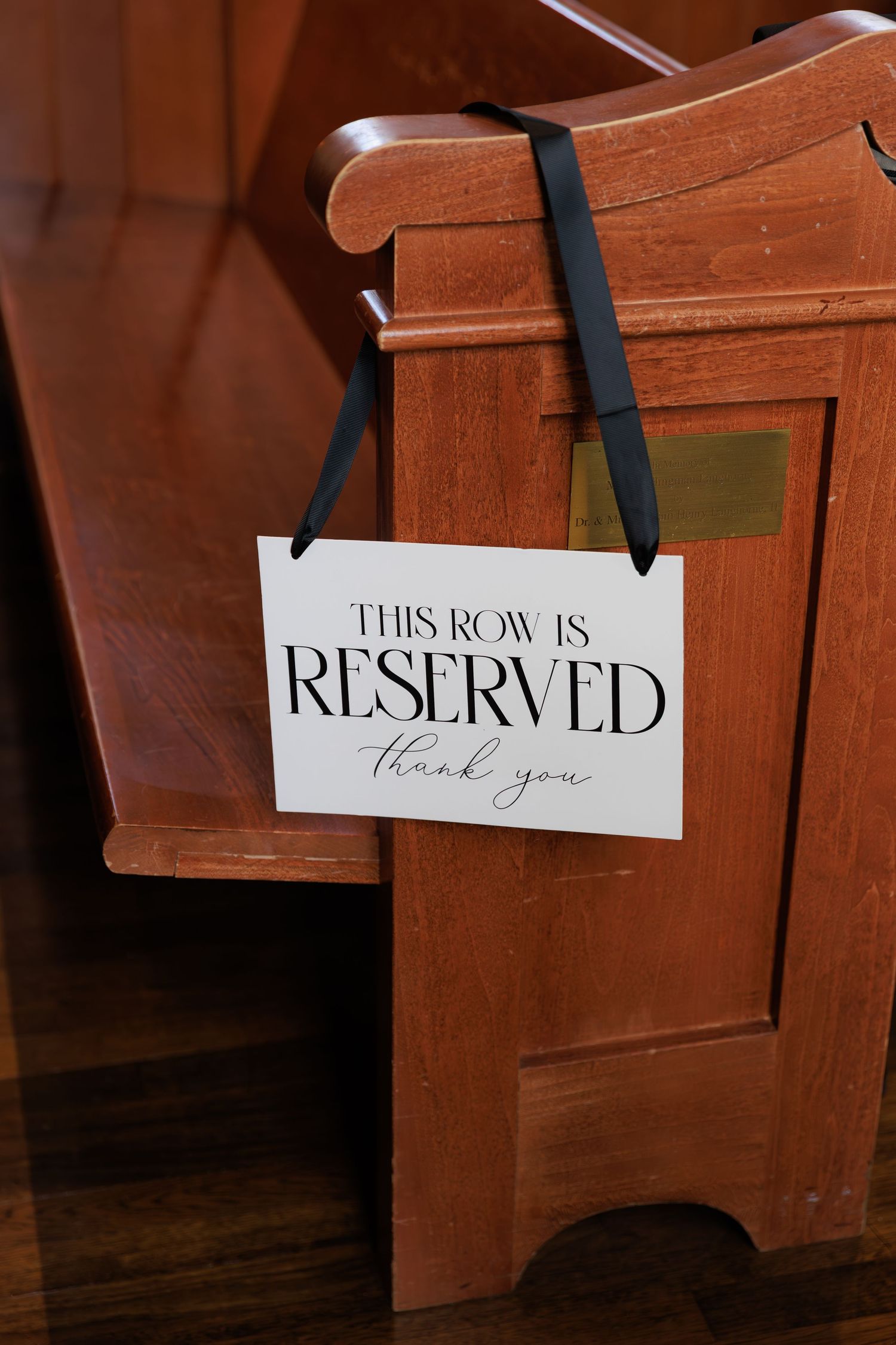 Wooden church pews with reserved seating signs attached by black ribbons for a special event.