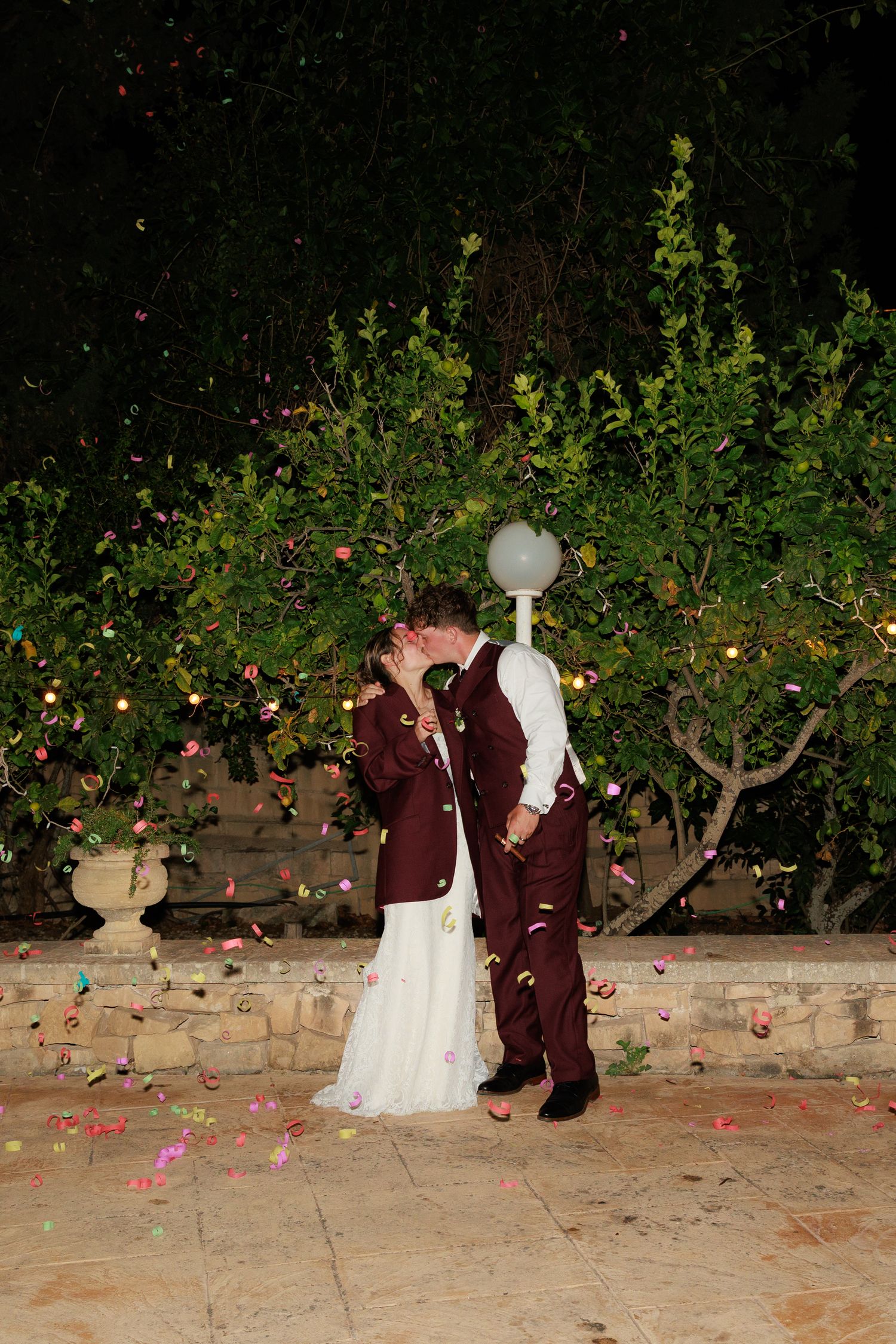 Romantic nighttime portrait of couple among rose petals and garden lights.