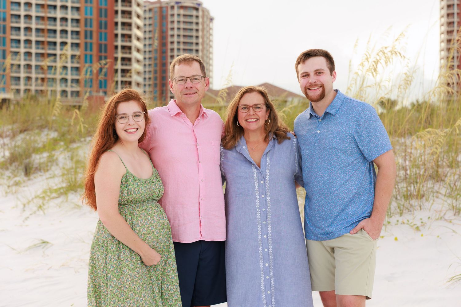 A group of people wearing coordinated pastel and blue outfits pose together on a sandy beach at sunset.