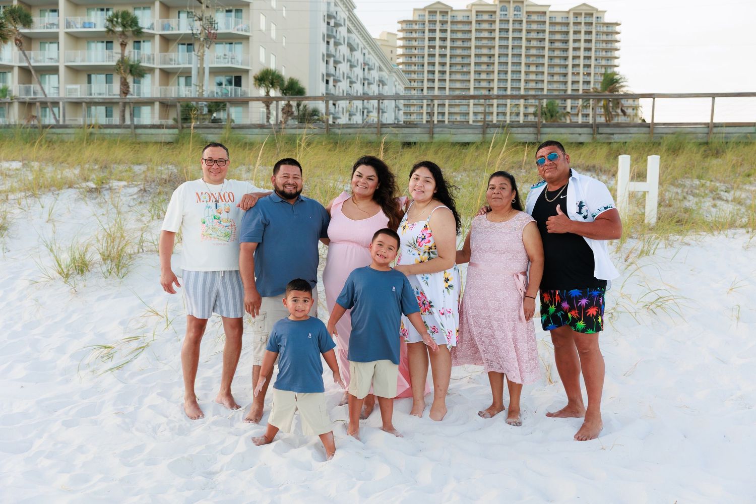 A group stands together on a white sandy beach with condominiums and palm trees visible in the background.