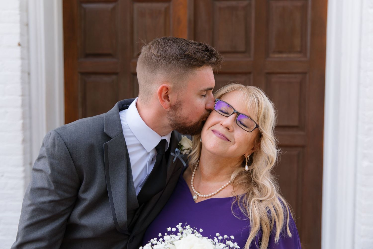 Tender moment captured between two people in formal attire outside church entrance.