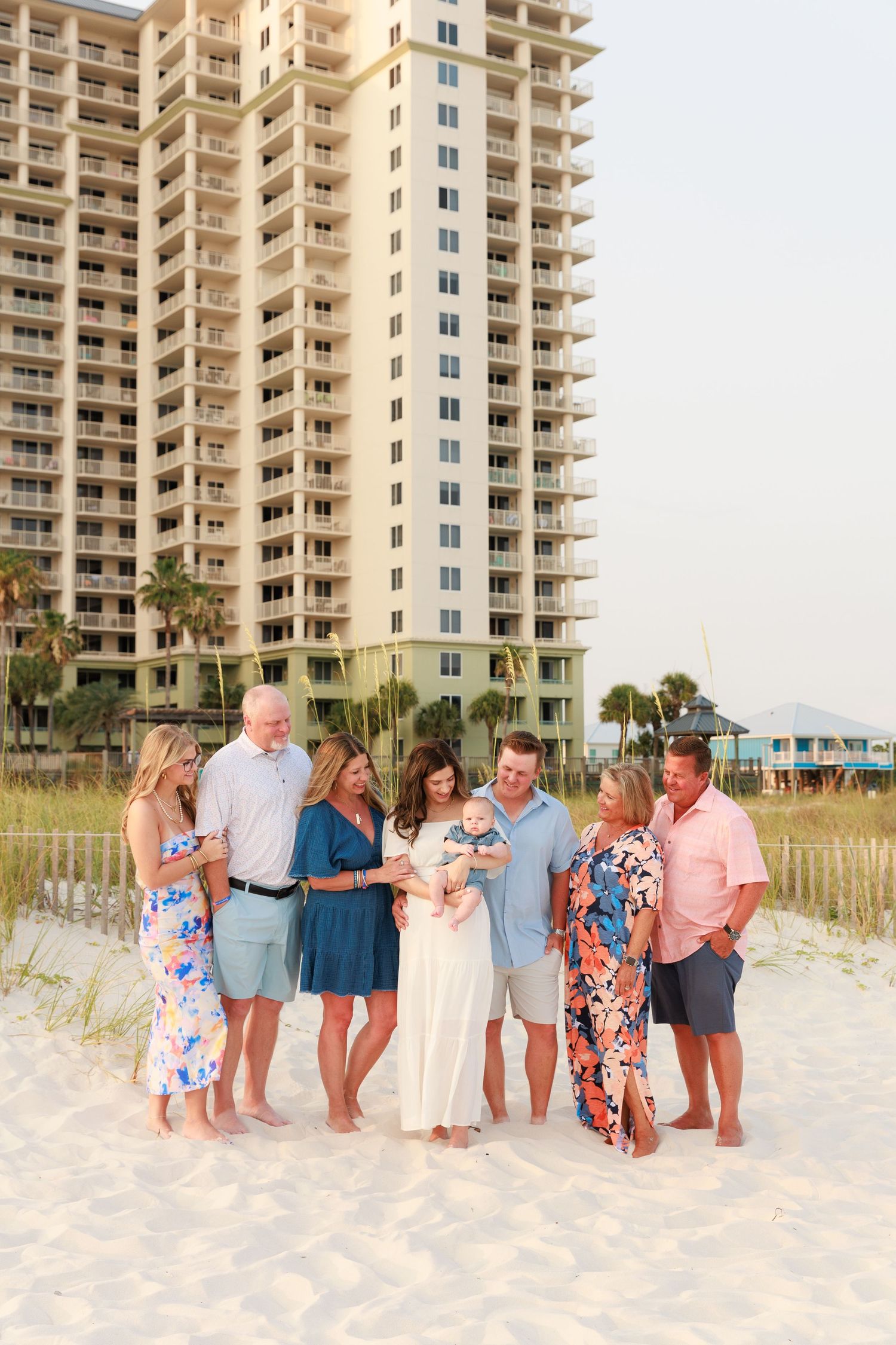 Family group photo on white sand beach with tall beachfront condo building backdrop during golden hour sunset.