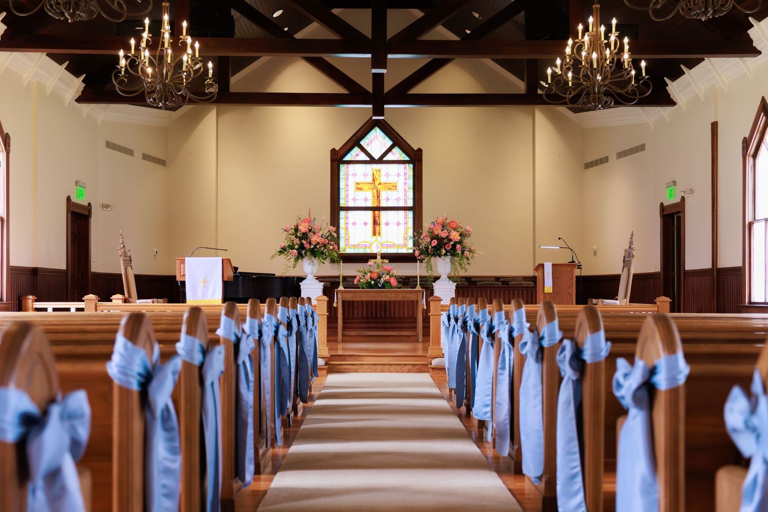 Church sanctuary with wooden pews adorned with light blue bows along the aisle leading to a chandelier-lit altar.