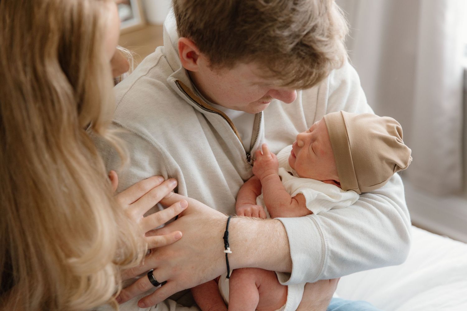 A tender moment between parent and newborn baby during a lifestyle photography session in a bright white room.