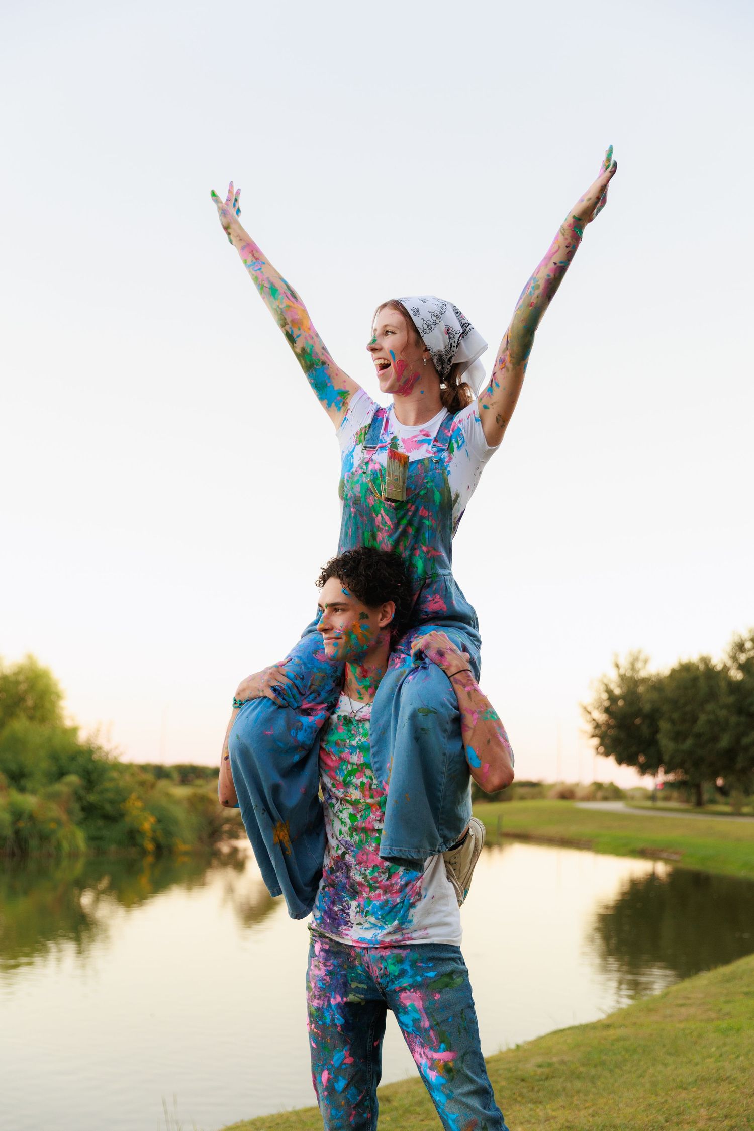 People in matching floral outfits pose joyfully by a lake at golden hour.