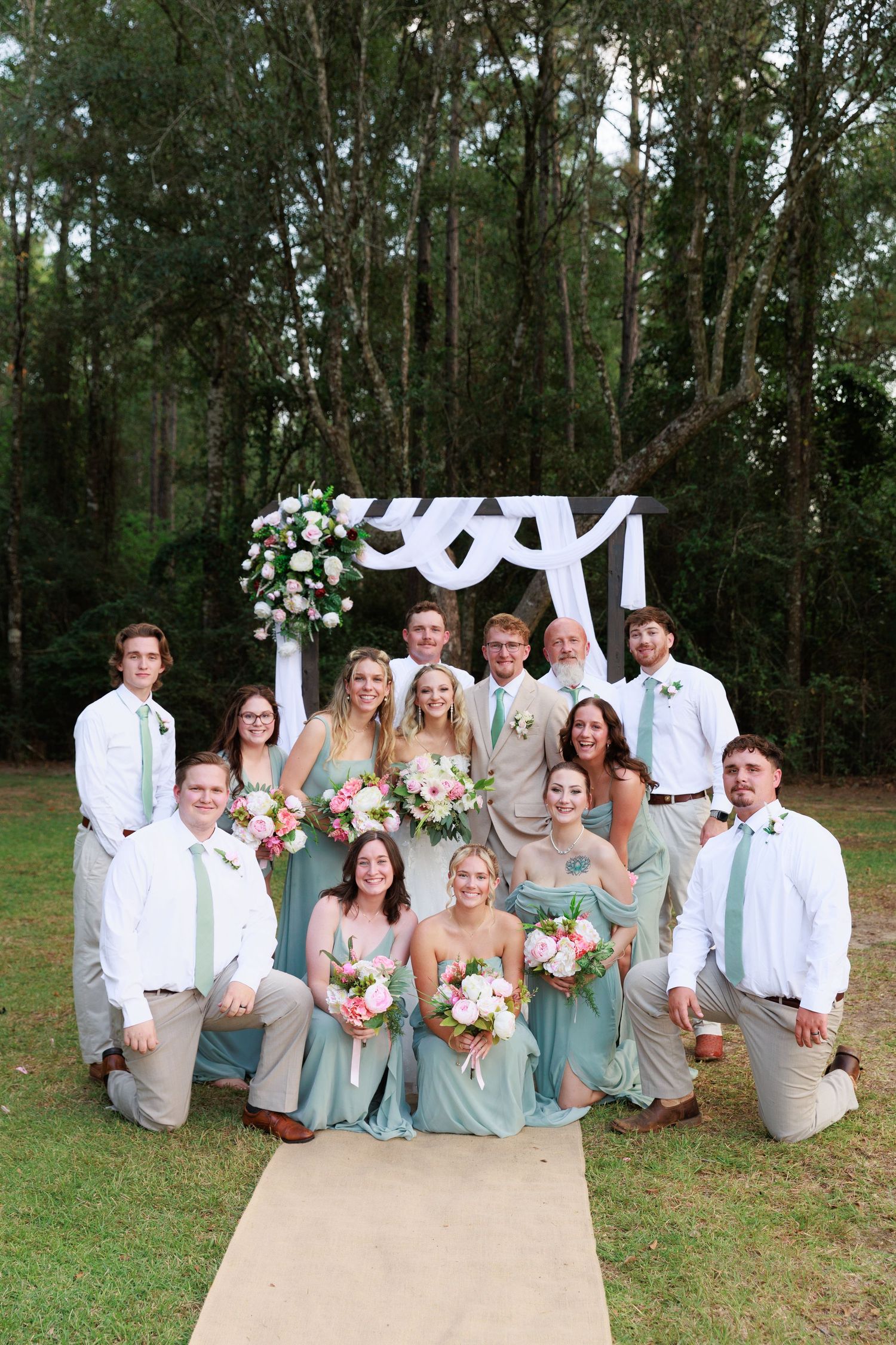 Wedding party in mint green dresses and white attire poses together on grass for outdoor group photos.