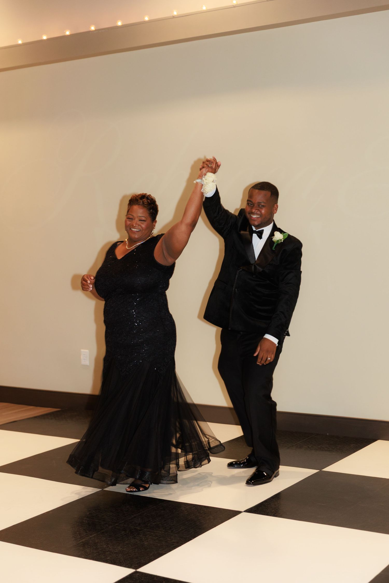 Wedding couple poses playfully on a geometric black and white dance floor with string lights overhead.