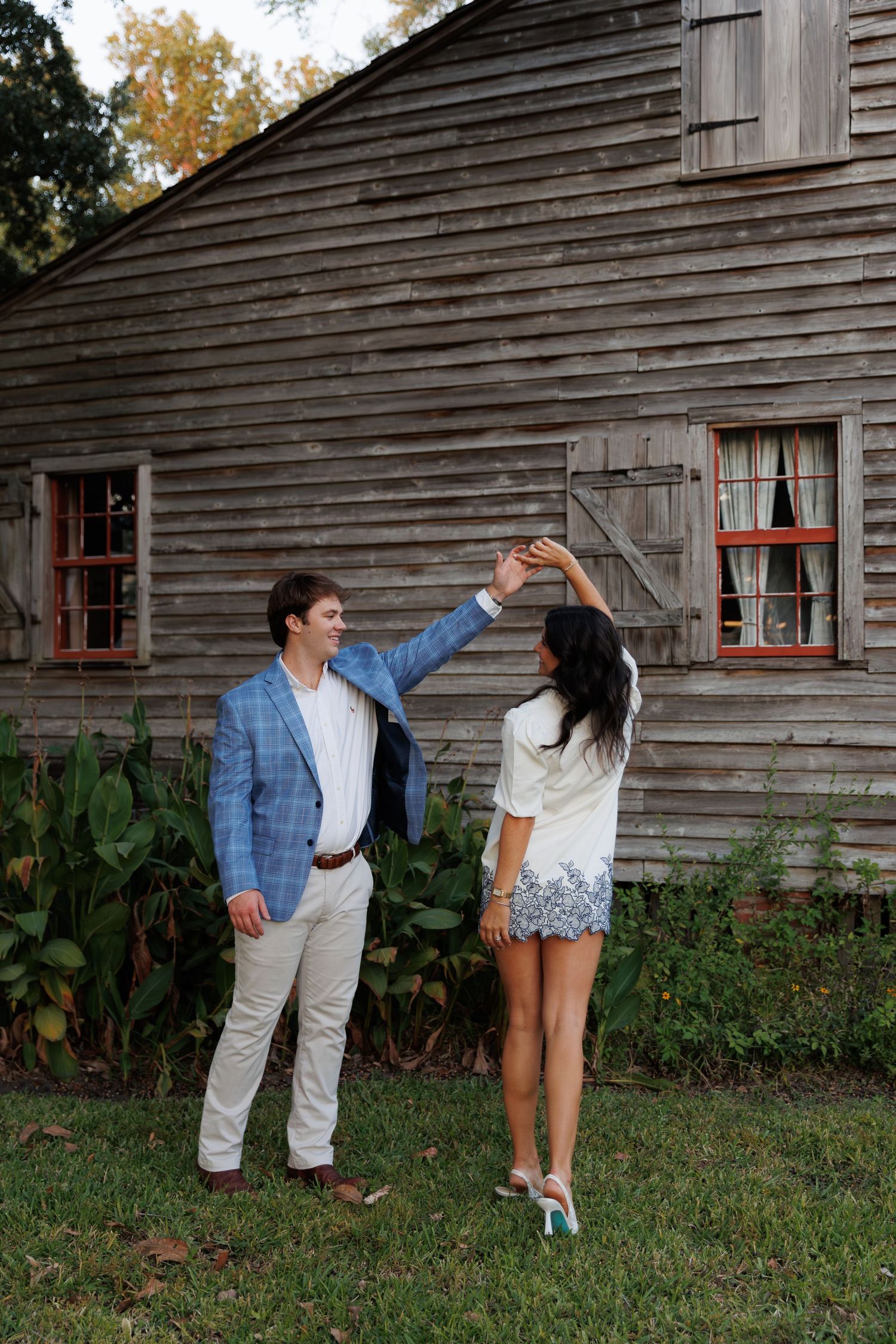 Dancing couple shares romantic moments near weathered barn with garden and autumn trees visible.