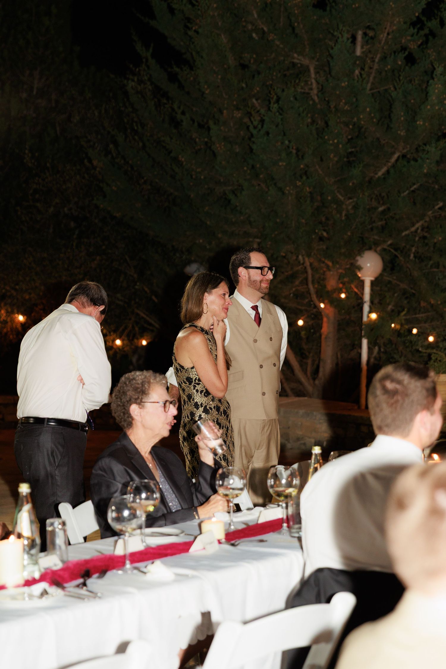 Guests seated at long tables during an outdoor evening reception with string lights illuminating the space.