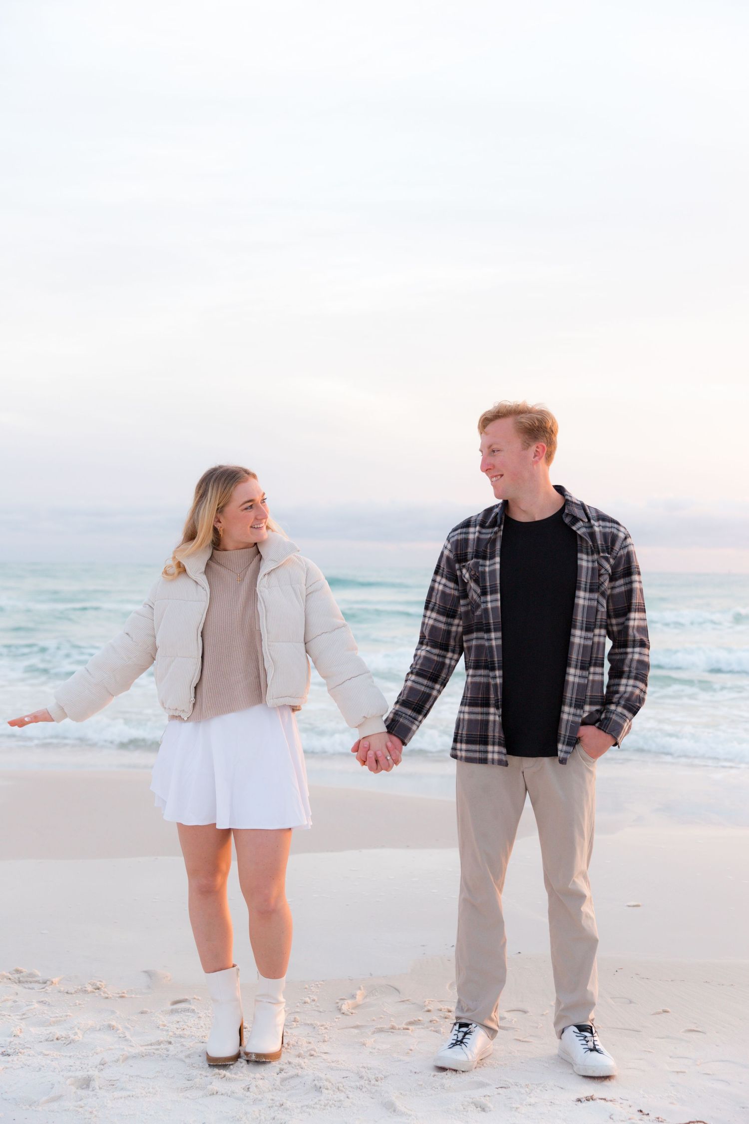 Two people playfully walking together on a white sandy beach by the ocean.