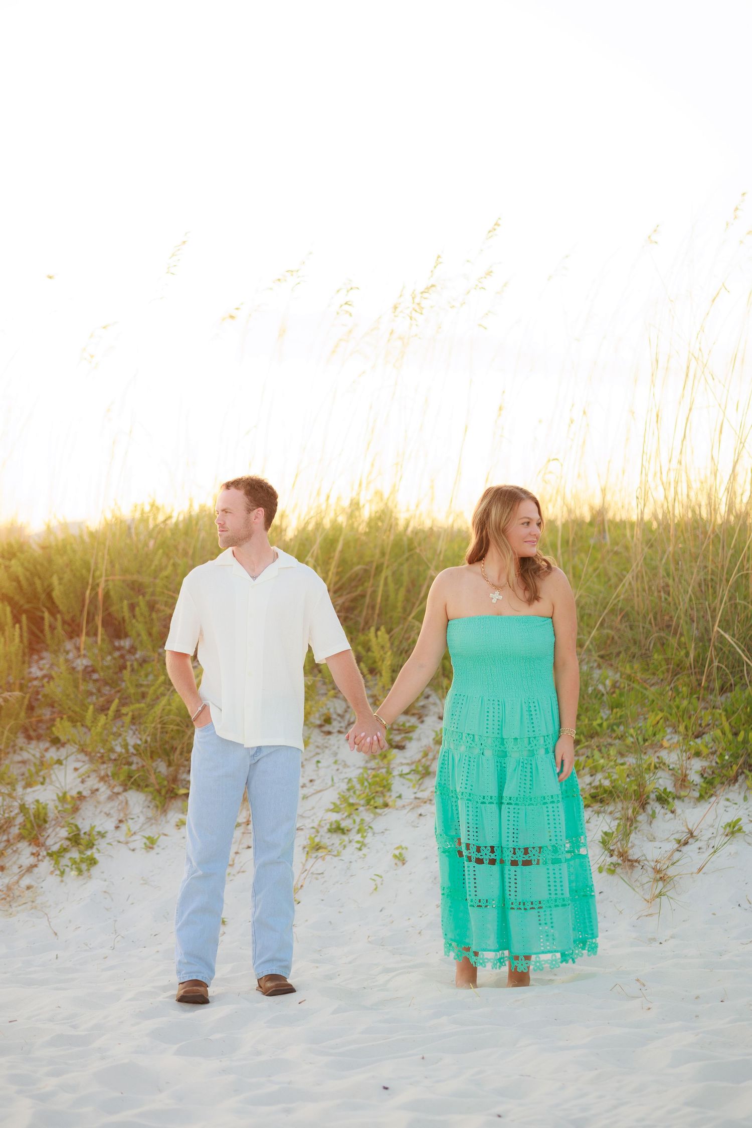 A couple walking hand in hand along a sandy beach with sea grass at sunset.