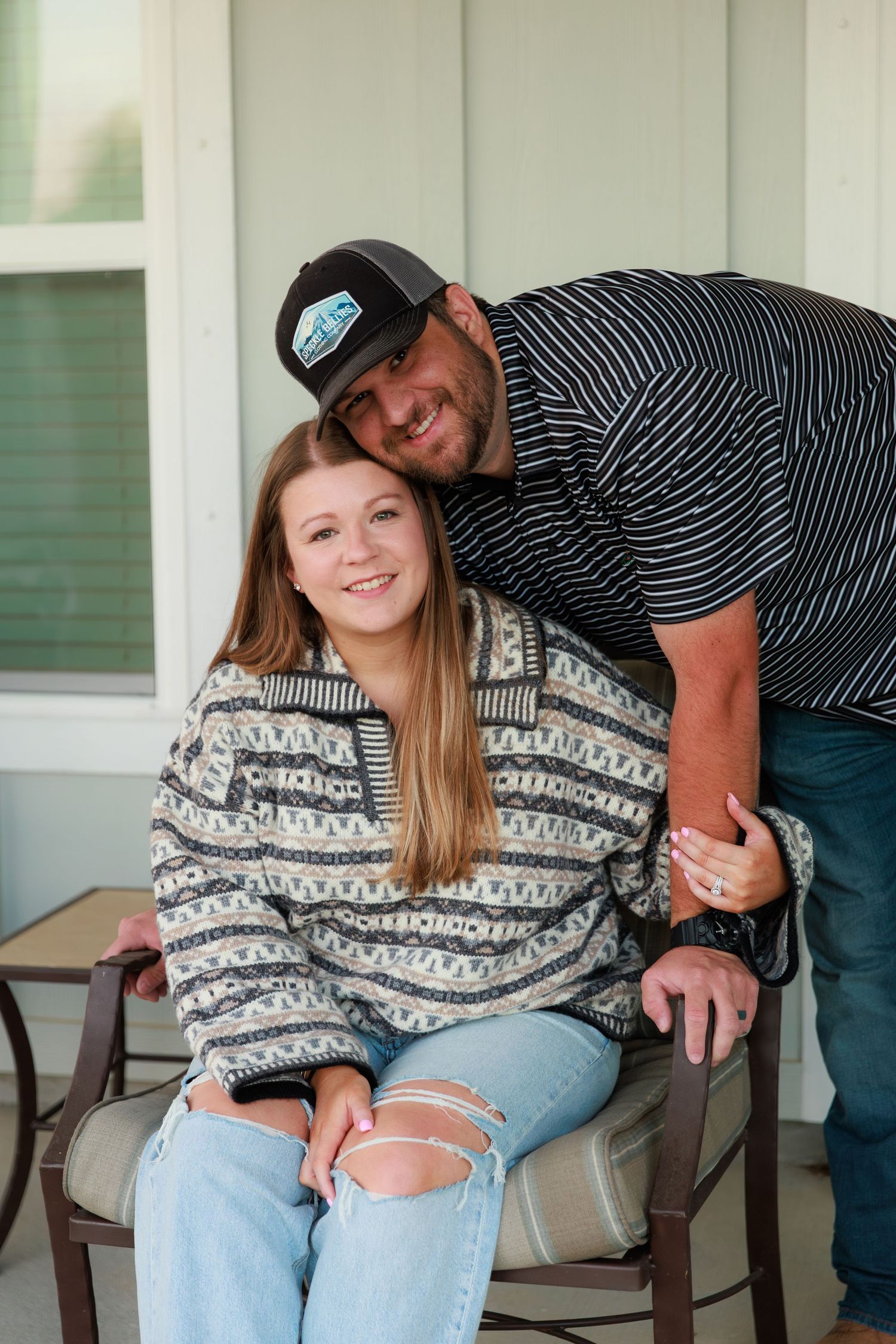 A couple in casual clothing share a sweet moment while sitting on their front porch bench.