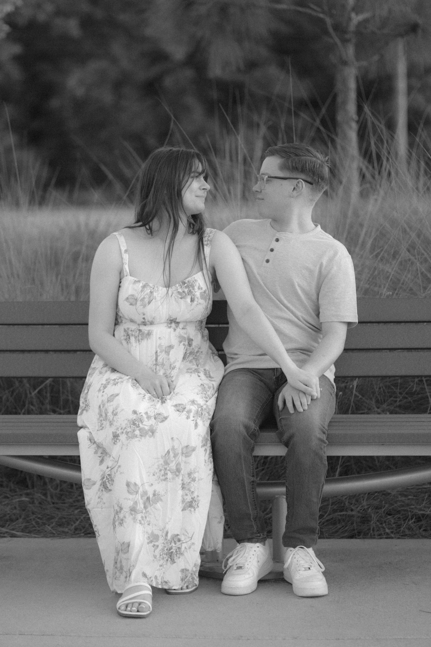 Couple sitting on a bench laughing together in black and white photo, woman in floral dress and man in henley shirt.
