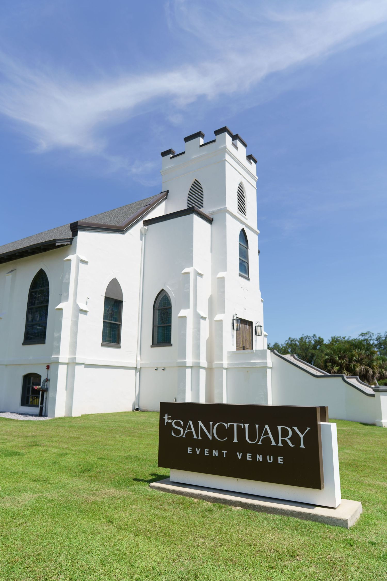 White church building converted into The Sanctuary Event Venue, featuring Gothic architecture and a tower against a blue sky.