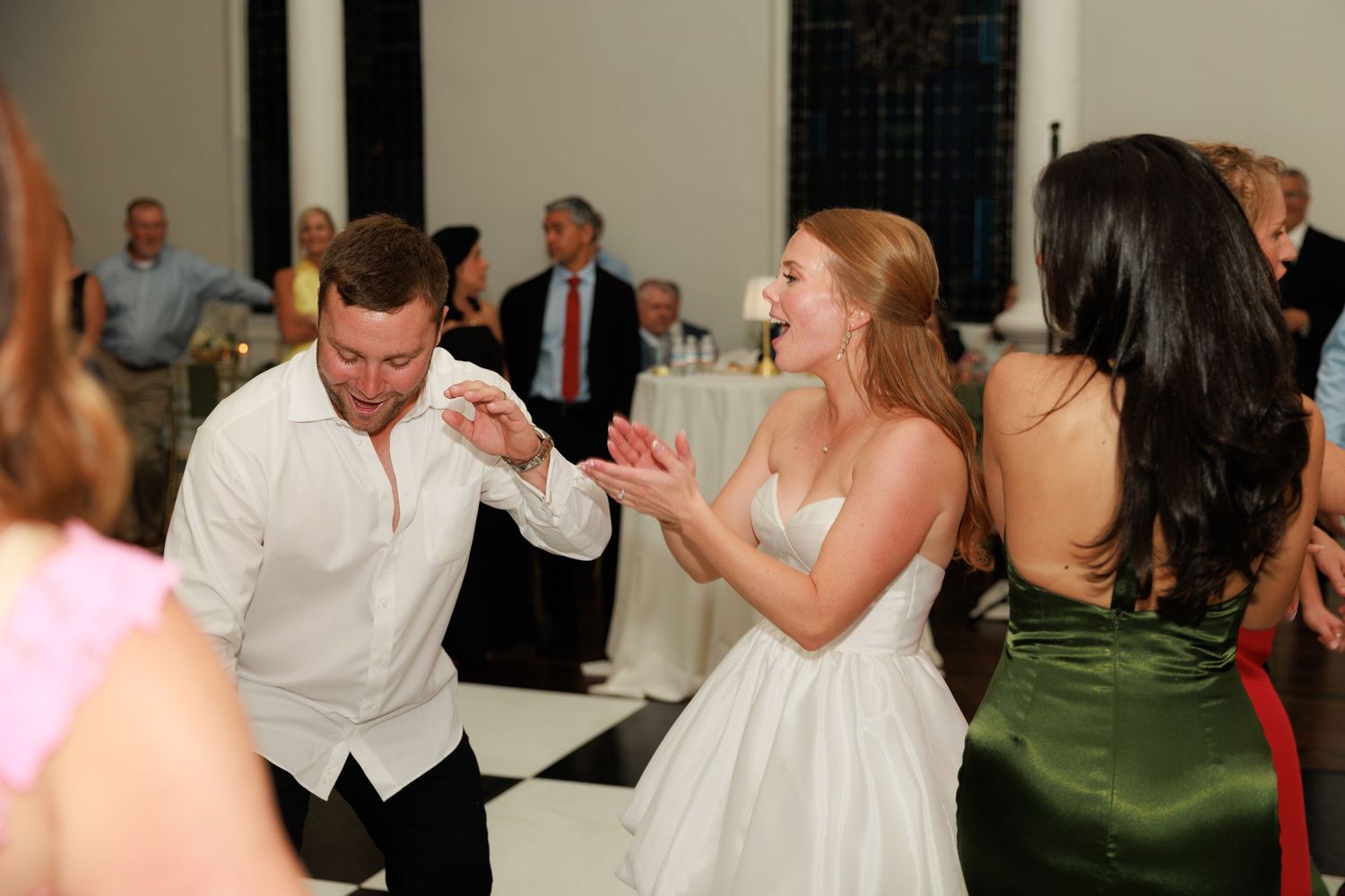 Bride and guests dancing joyfully on the white dance floor during a lively wedding reception celebration.