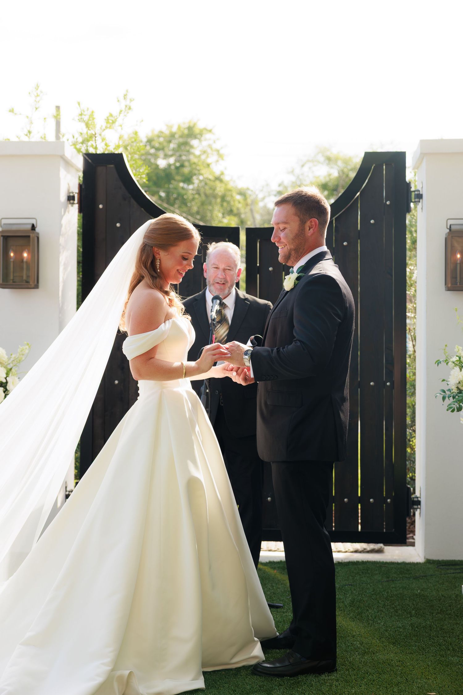 Bride places ring on groom's finger during outdoor wedding ceremony.