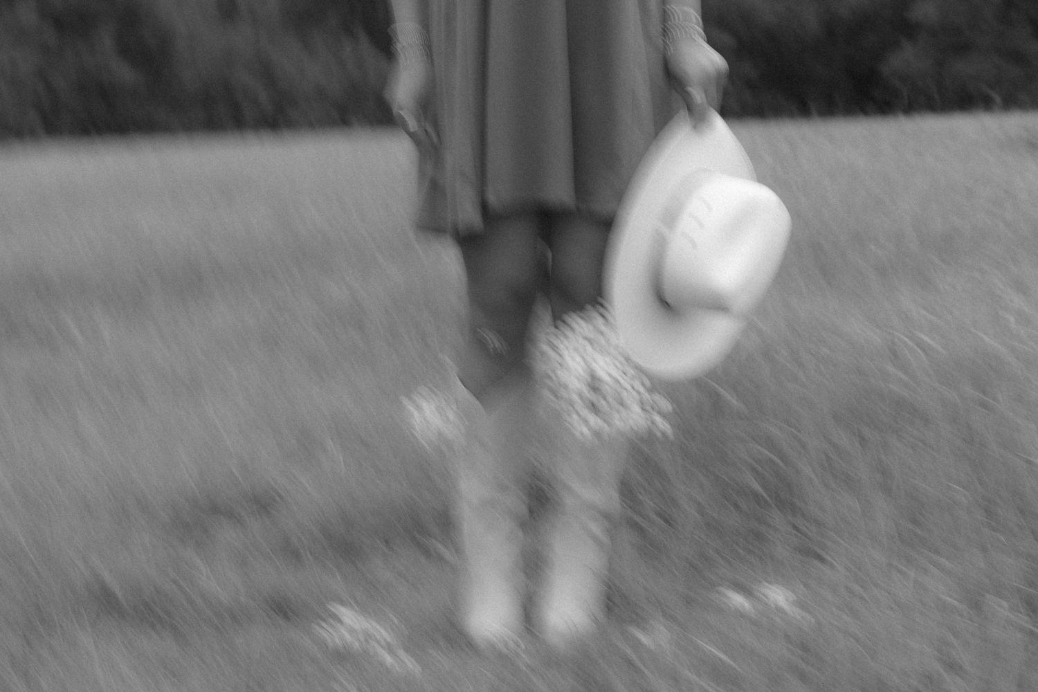 Blurred artistic black and white photo showing a person in boots holding a hat.