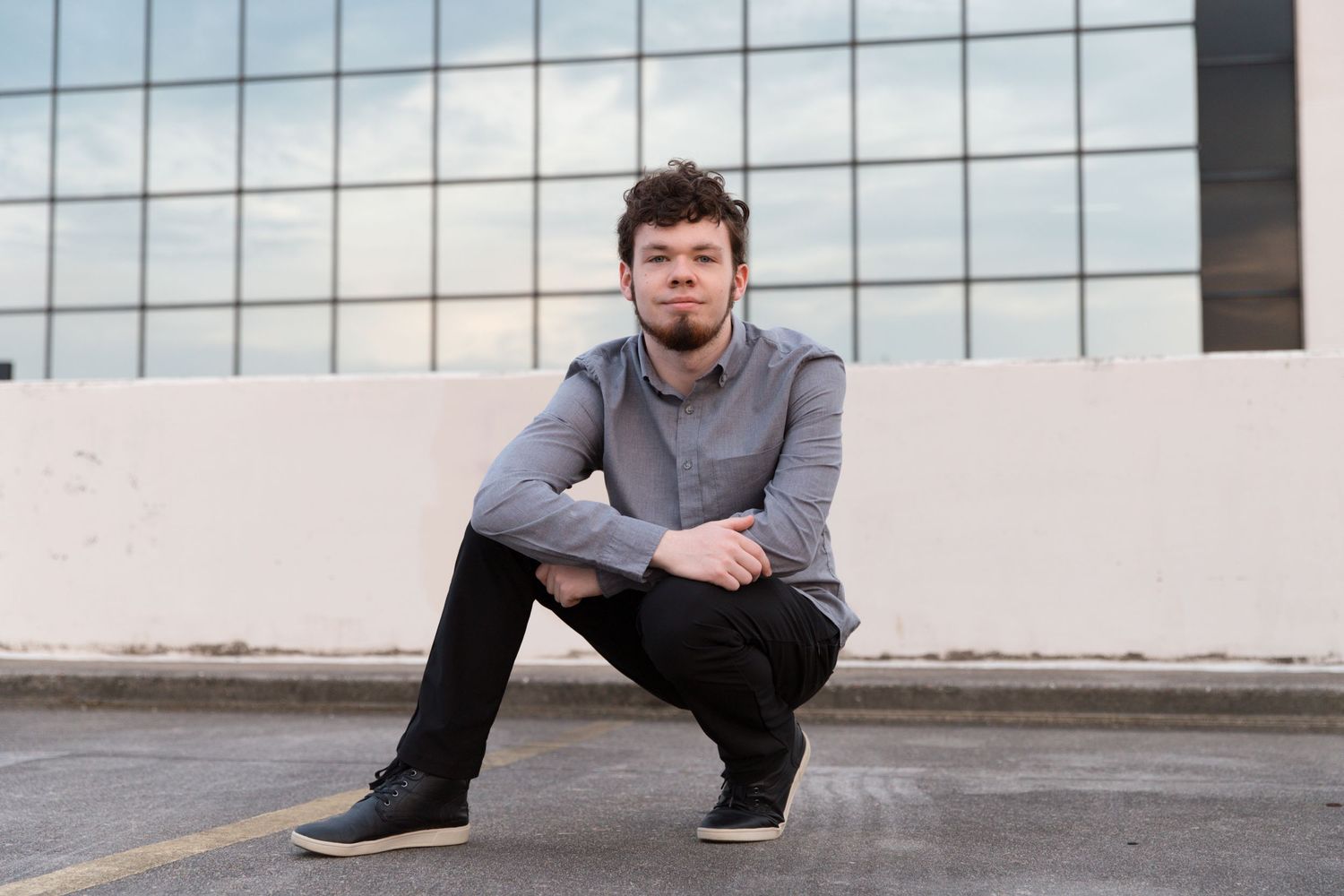 Urban fashion portrait crouching against white wall with glass building background.