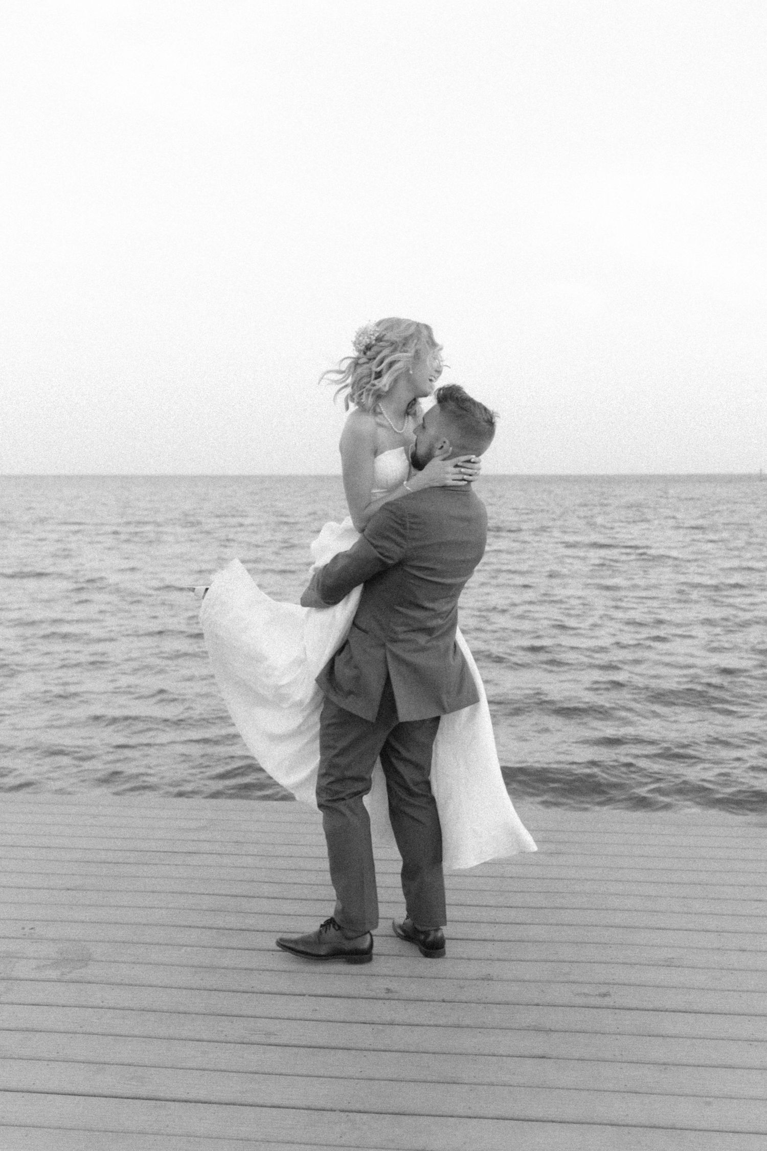 Black and white photo of romantic embrace on seaside dock.