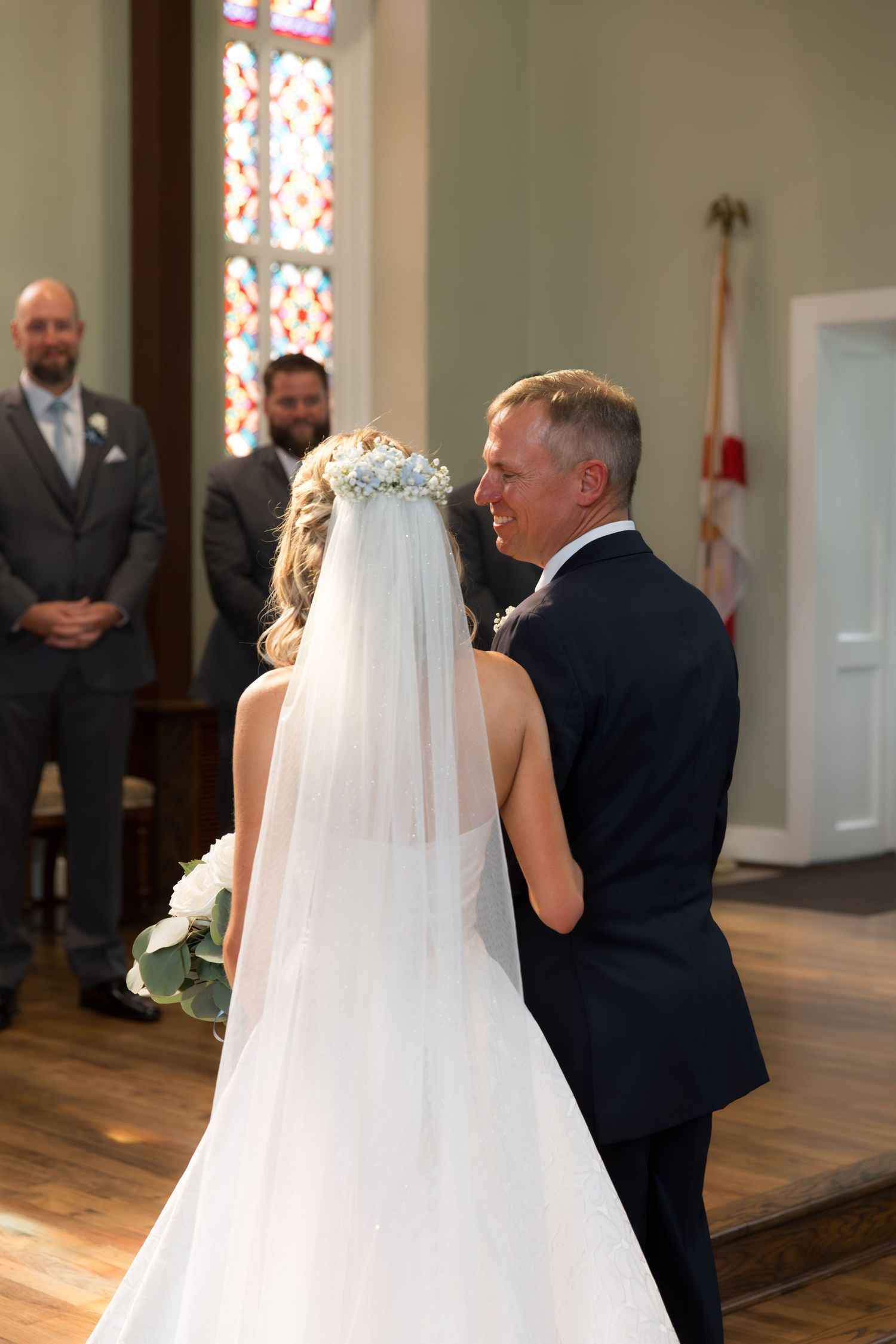 Wedding ceremony in progress inside traditional church with stained glass windows.