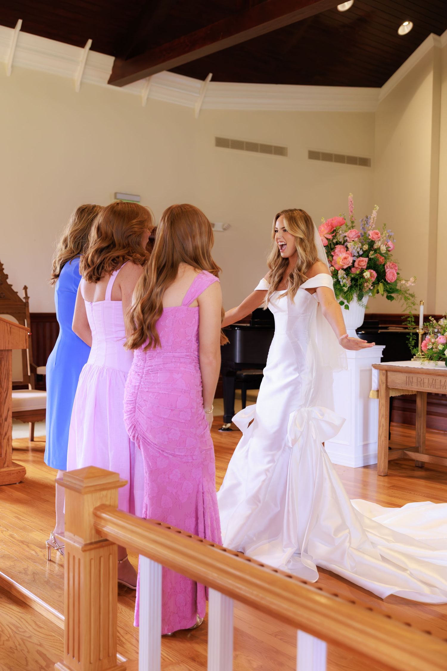 Bridesmaids in colored dresses gather around bride in white gown during wedding ceremony in church.