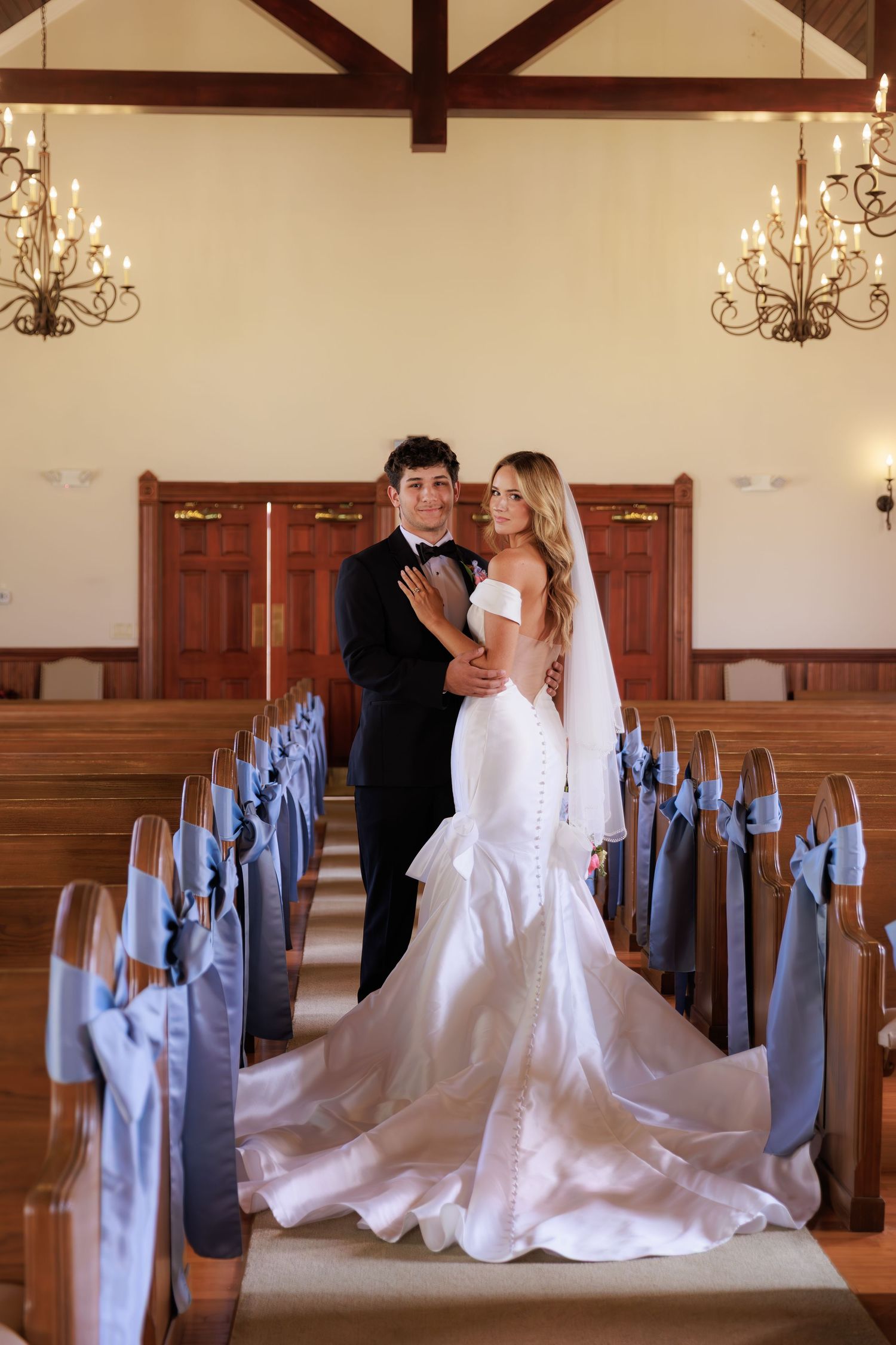 A wedding couple poses in a church with light blue chair decorations and wooden pews in a romantic photo sequence.