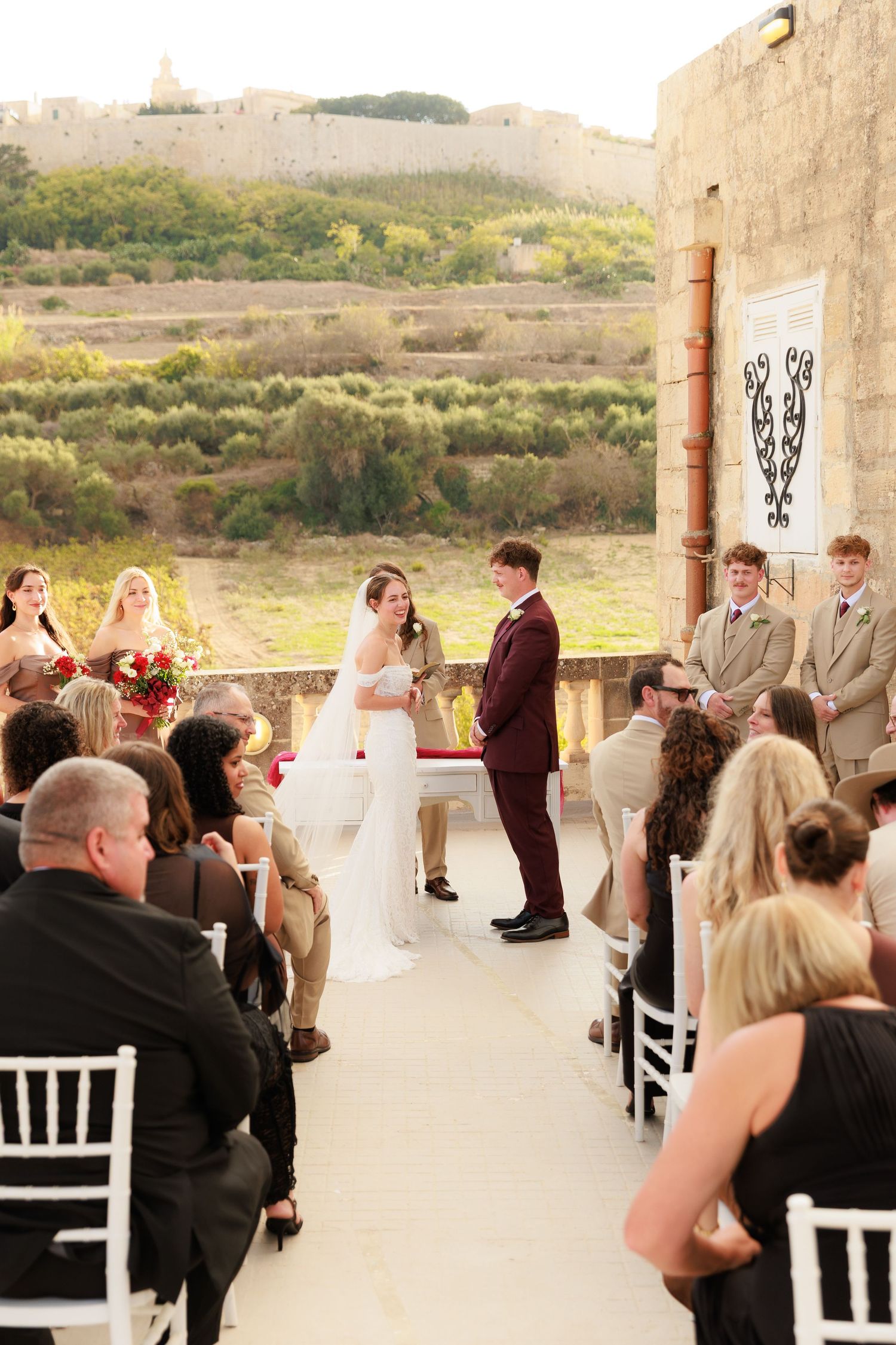 Outdoor wedding ceremony setup with white chairs and stone columns against a scenic natural backdrop.