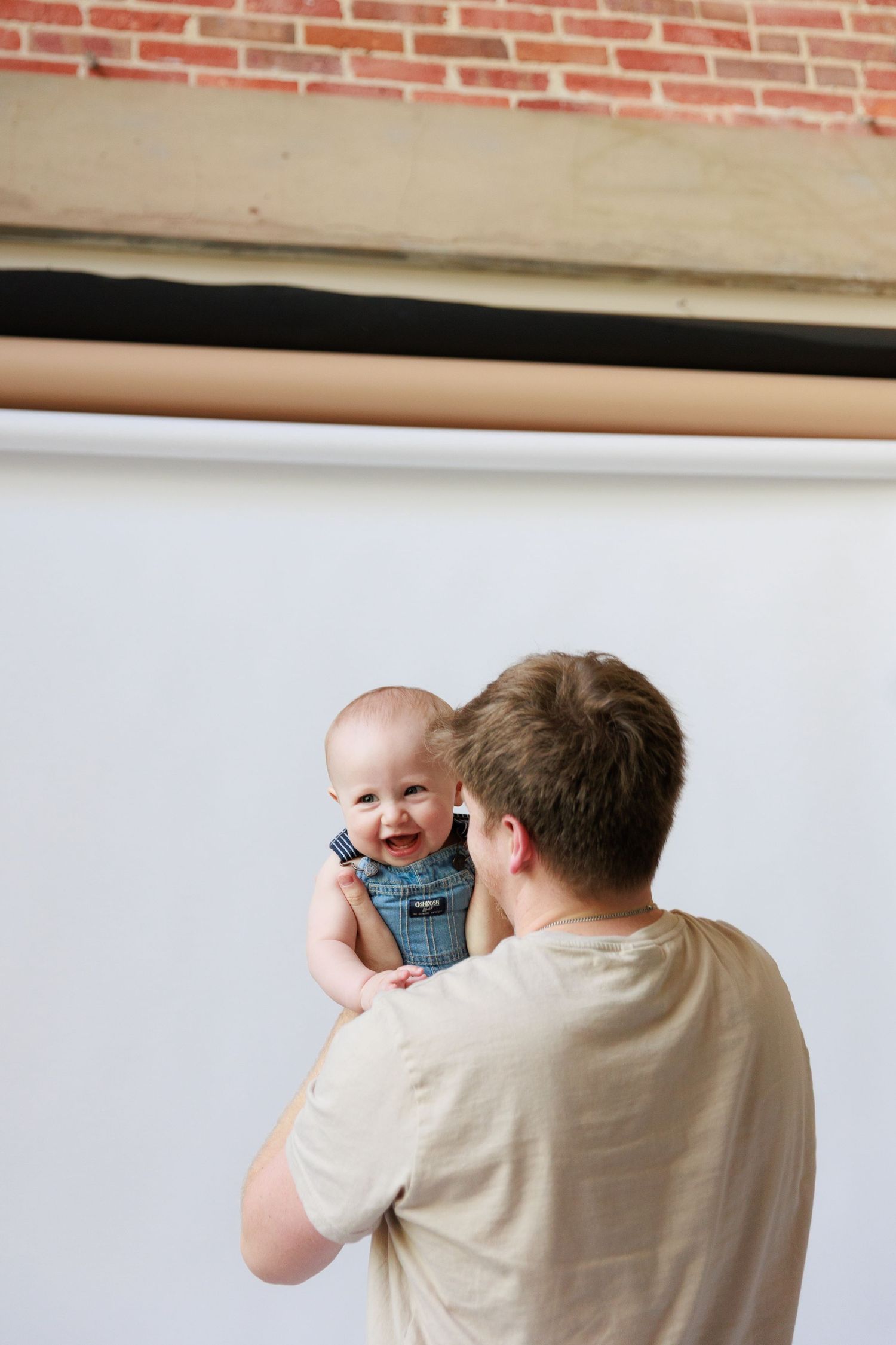 A photographer takes photos of a baby wearing a plaid shirt against a white backdrop.