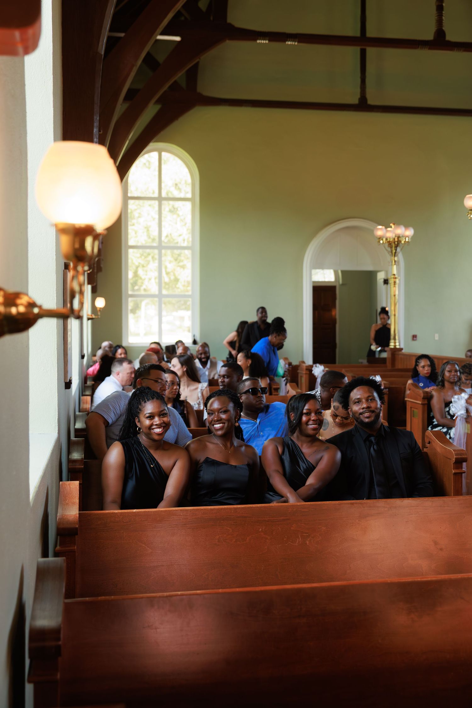 Wedding guests smile and celebrate from wooden church pews during a joyous ceremony.