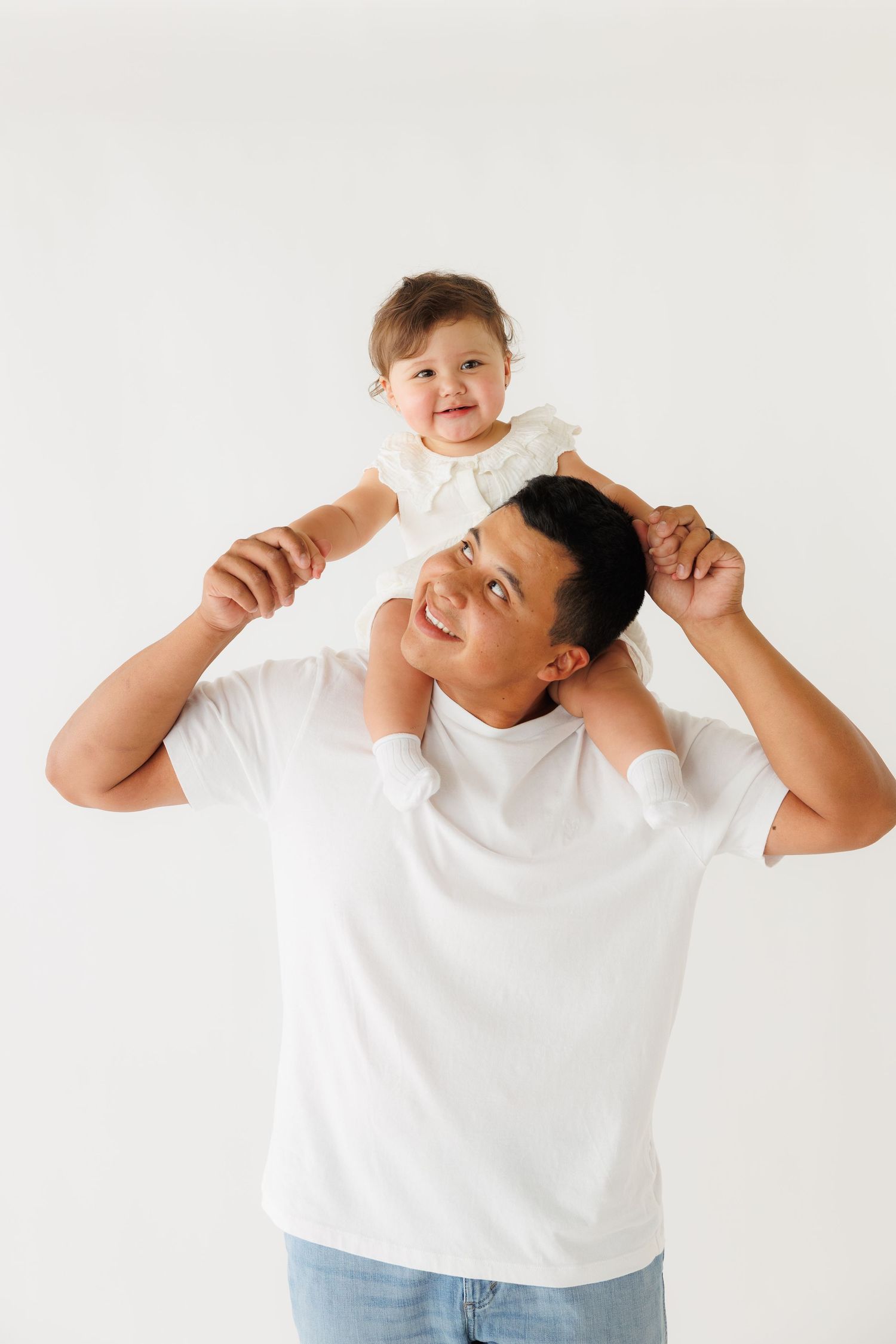 Smiling father holding baby girl on his shoulders against white background.