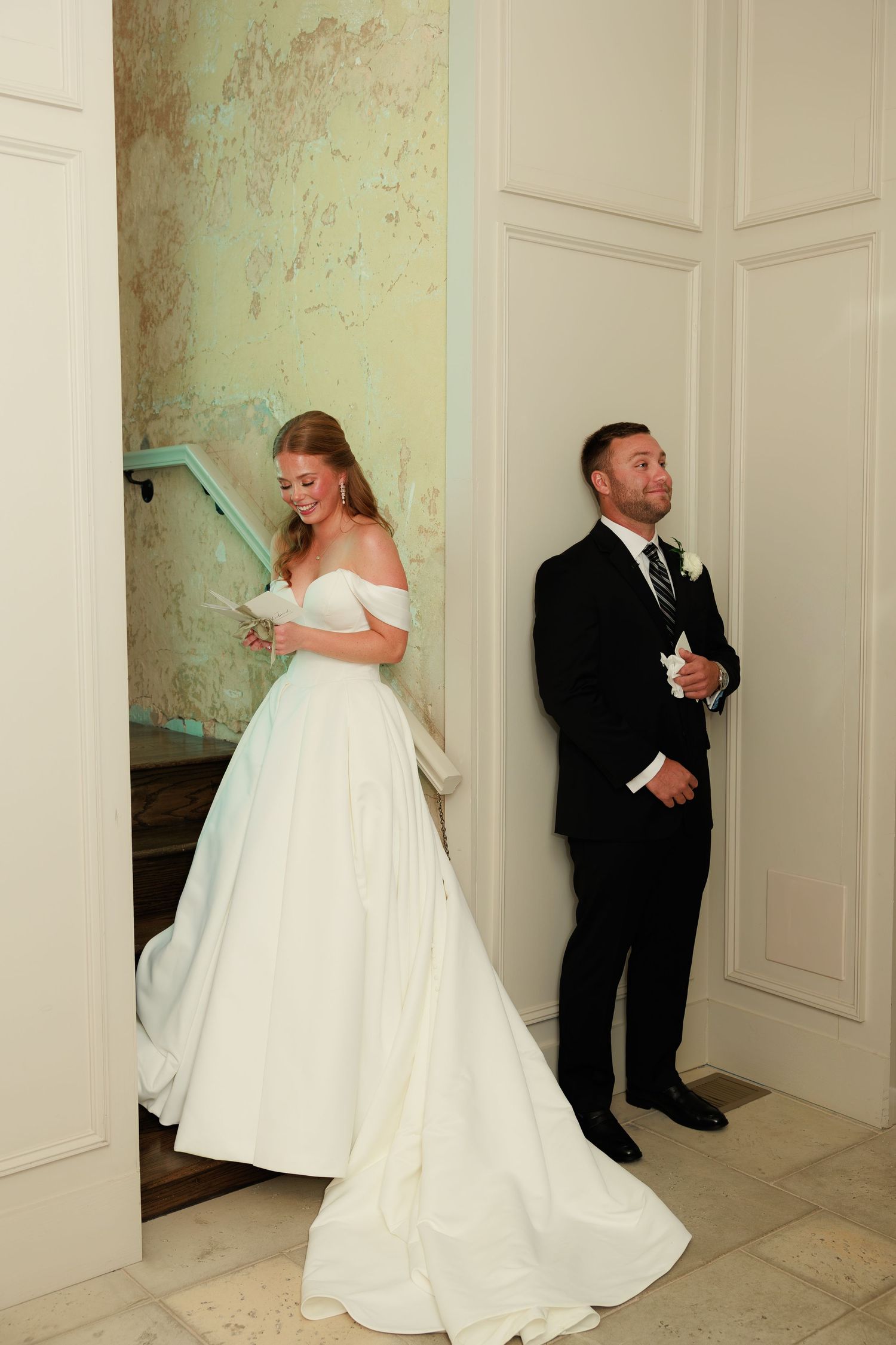 Bride in off-shoulder white ball gown and groom in black suit share a sweet pre-ceremony first listen moment.
