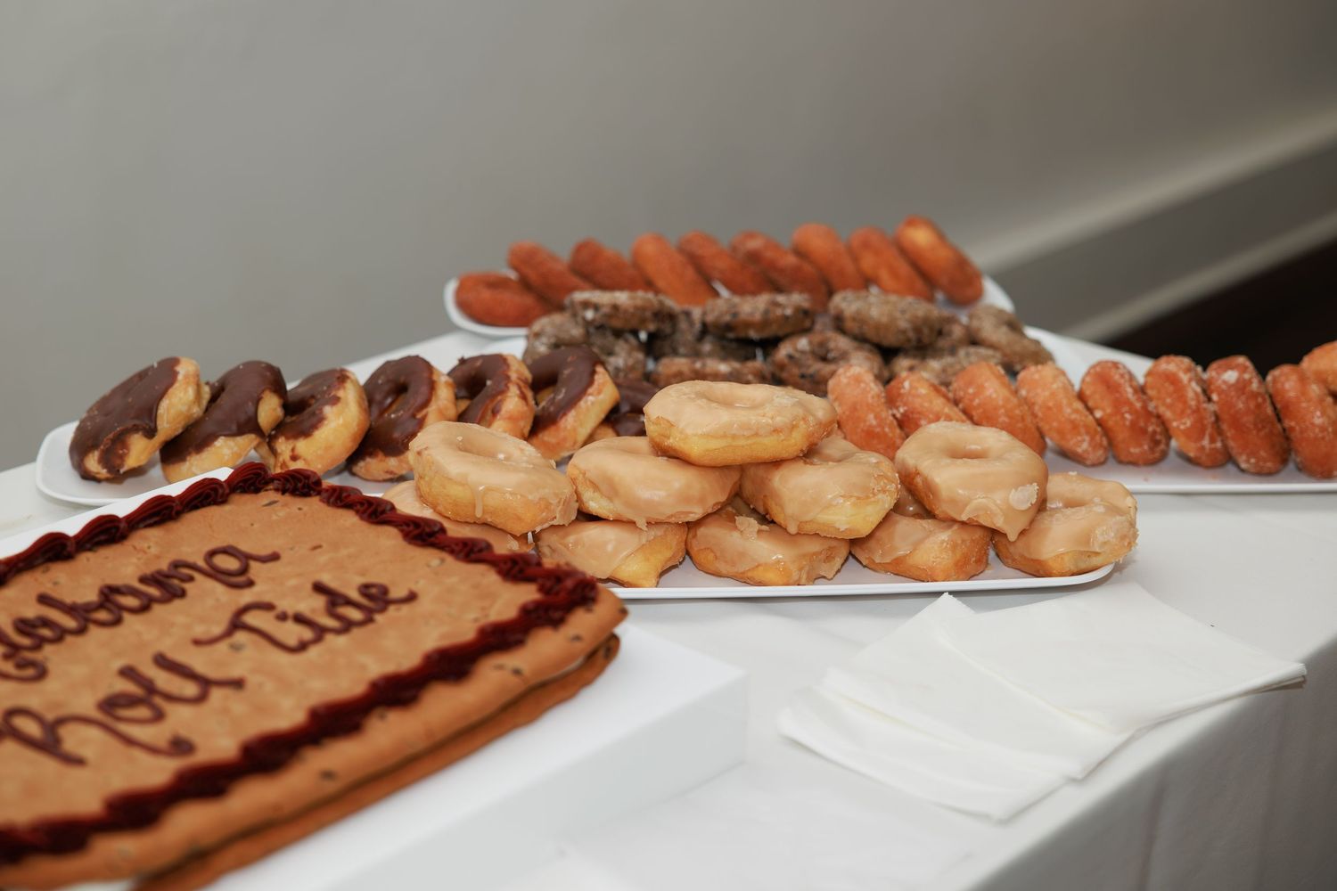 Assorted pastries and donuts on silver trays beside an Alabama Roll Tide decorated sheet cake.